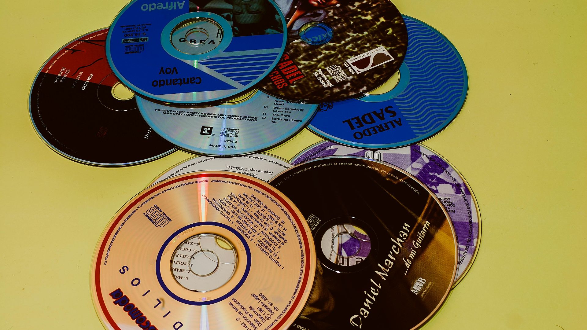 Flat lay of various CDs on a vibrant yellow surface, showcasing music diversity.