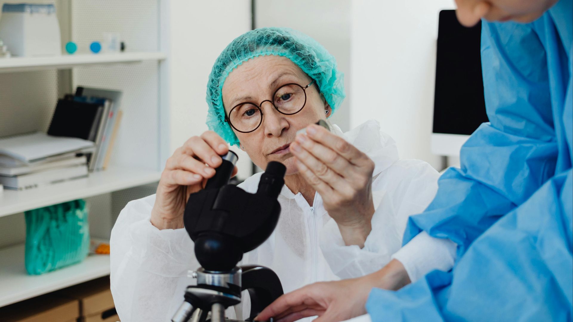 Researchers using microscope in a medical lab setting, equipped with protective gear and scientific tools.