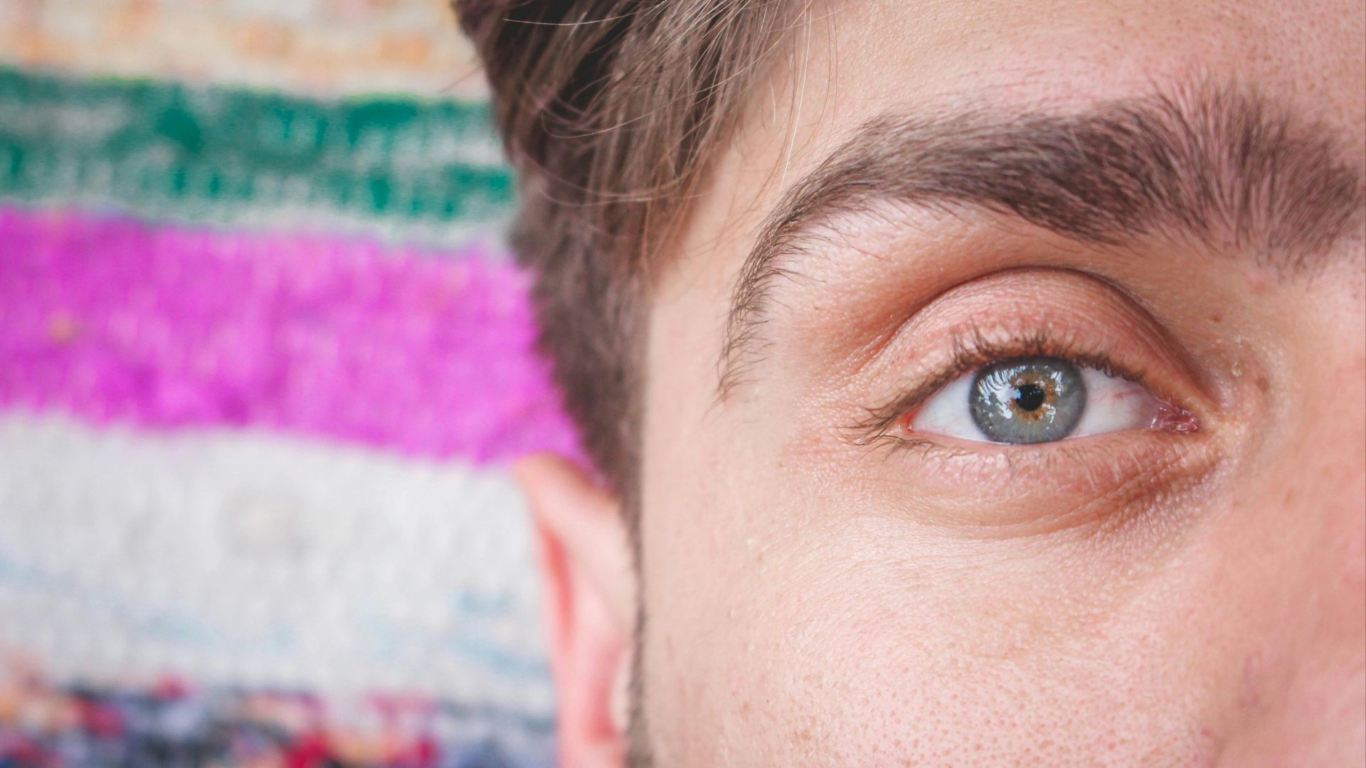 Detailed close-up of a man's blue eye with colorful textile backdrop.
