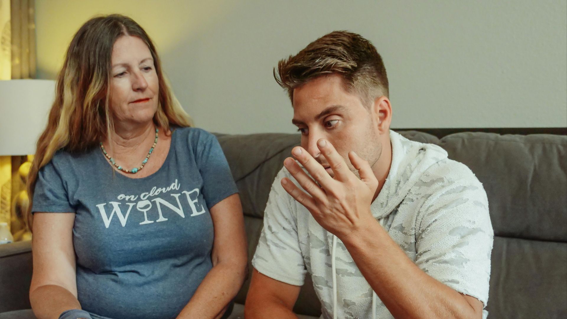 A mother and son engage in a deep conversation on the living room couch, conveying strong emotions.