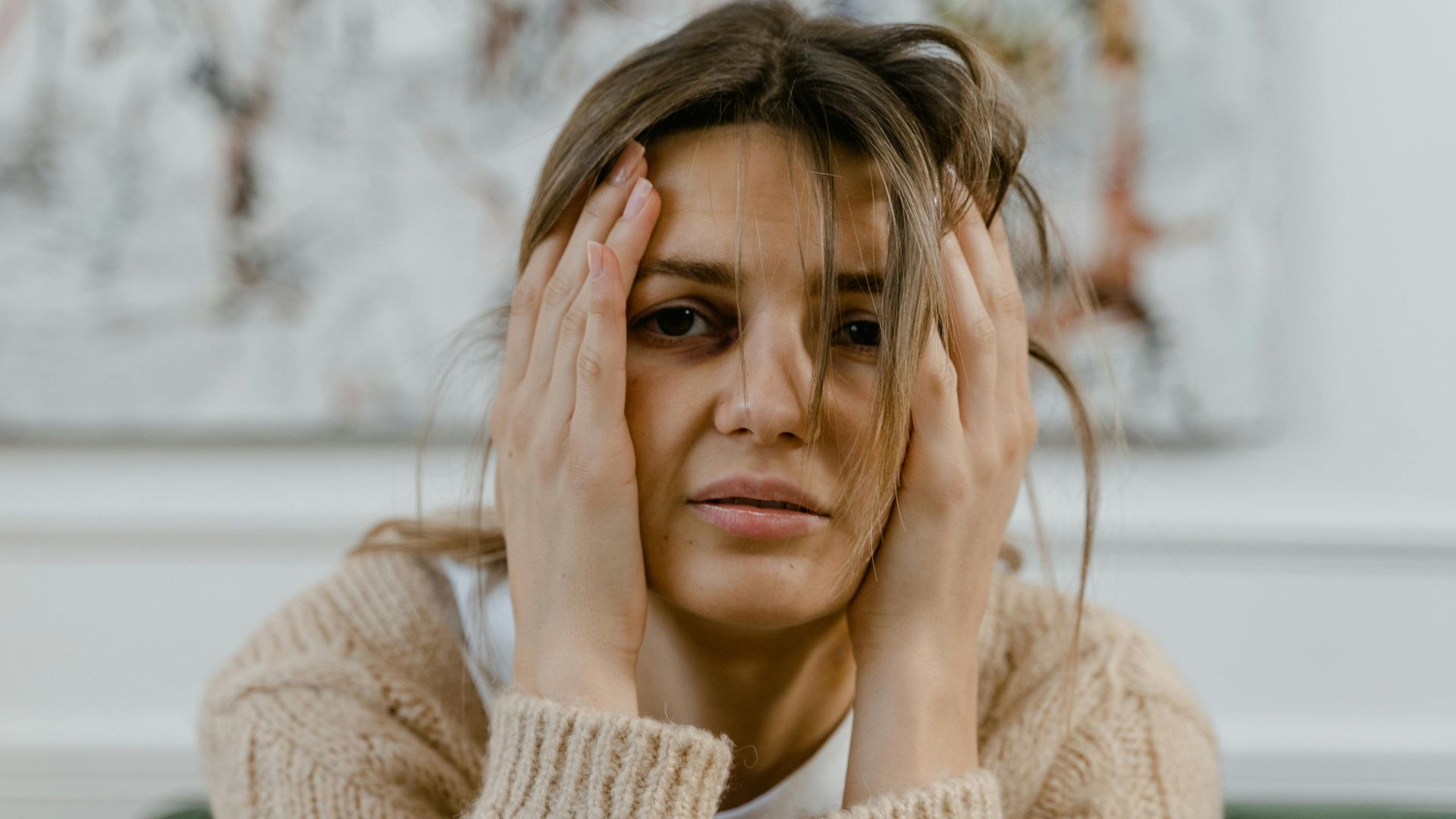 Woman looking distressed with hands on head, expressing worry indoors.