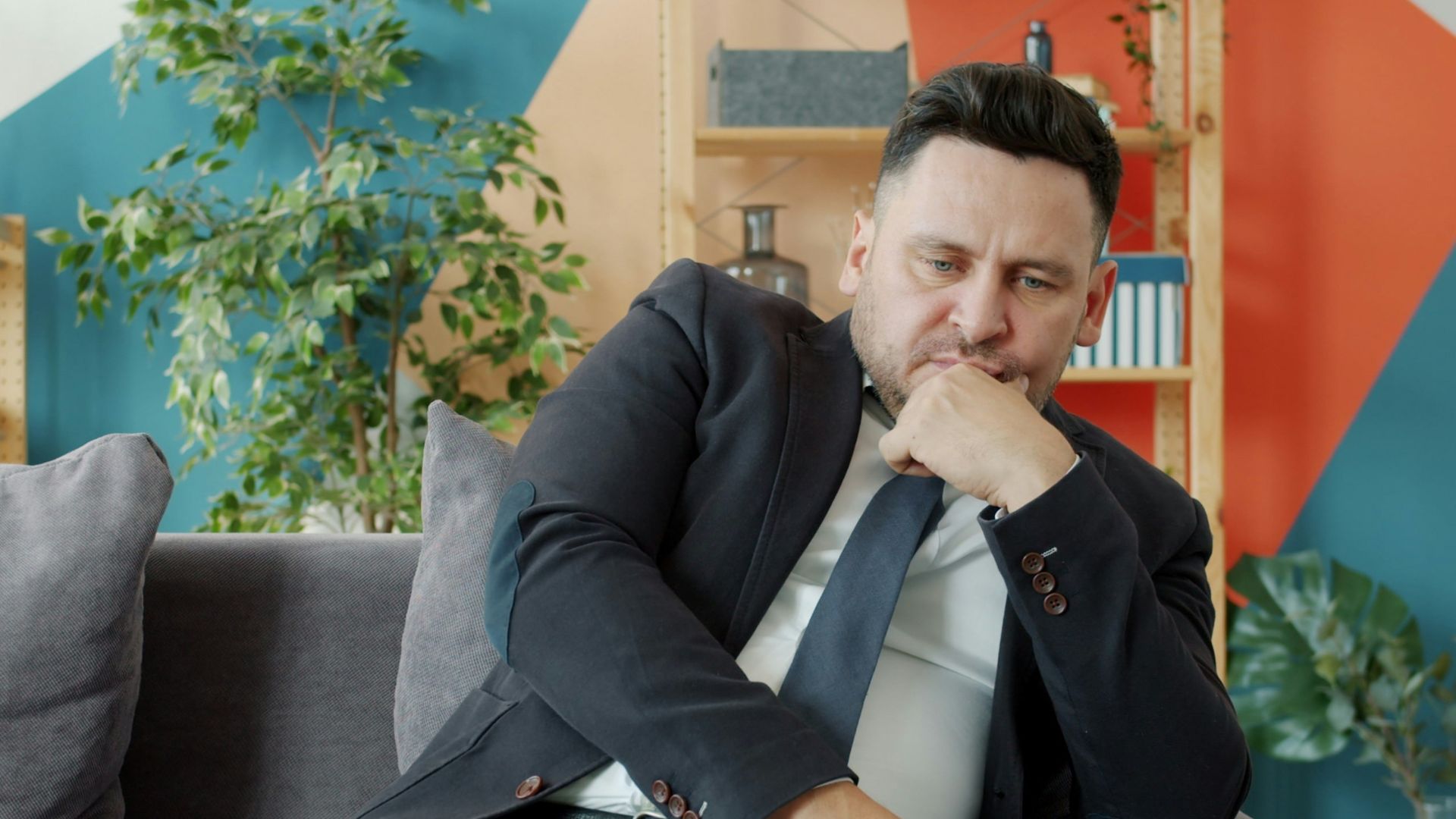 Man in suit sitting on couch looking thoughtful.