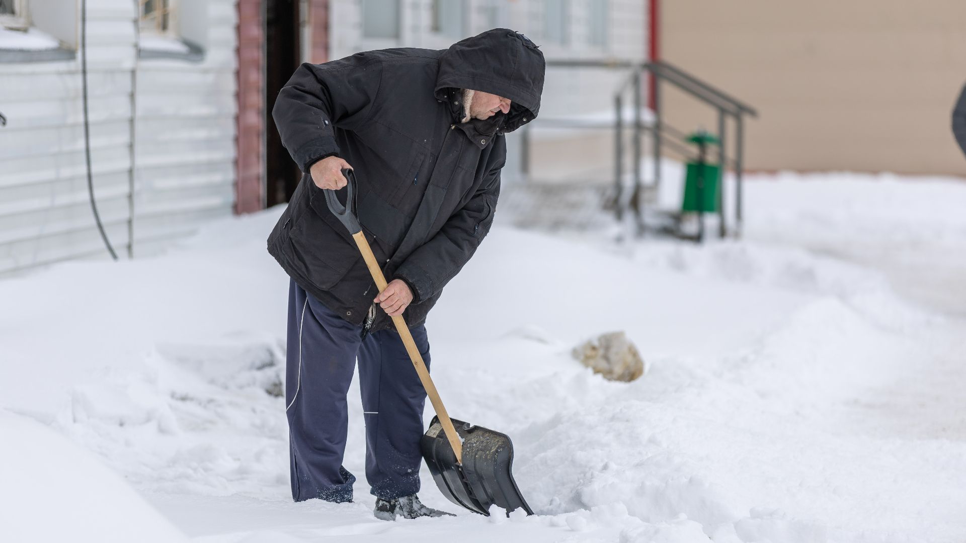 Adult man clearing snow with a shovel during a cold winter day, showcasing winter weather activities.