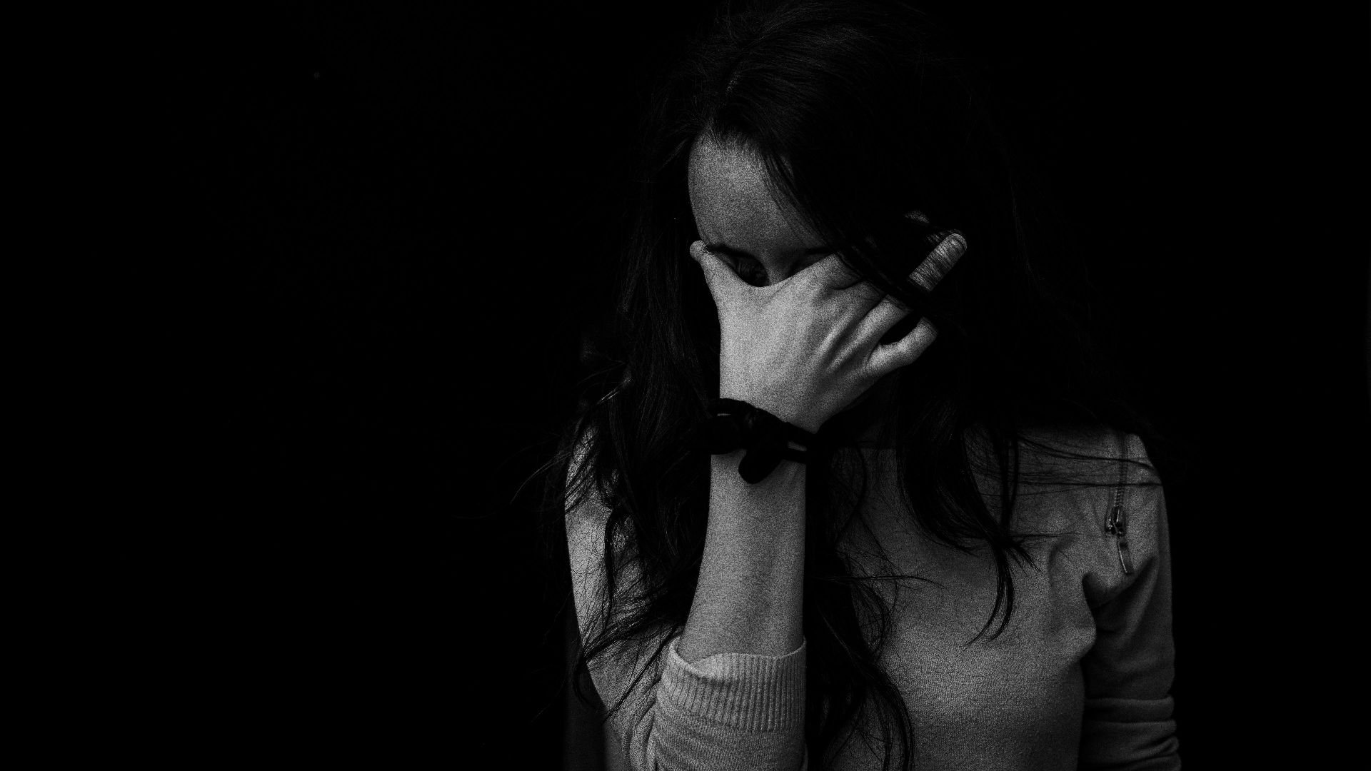 Intense black and white portrait capturing the emotion and introspection of a woman covering her face.