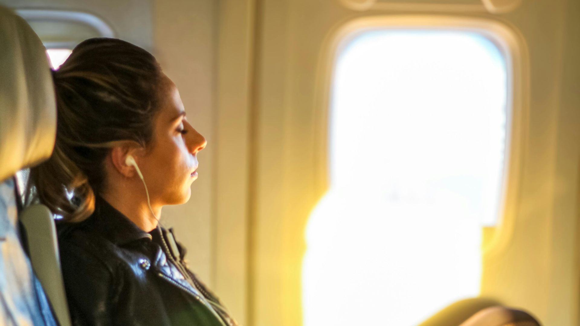 A woman enjoys a tranquil moment on a flight, gazing out the window with headphones on.