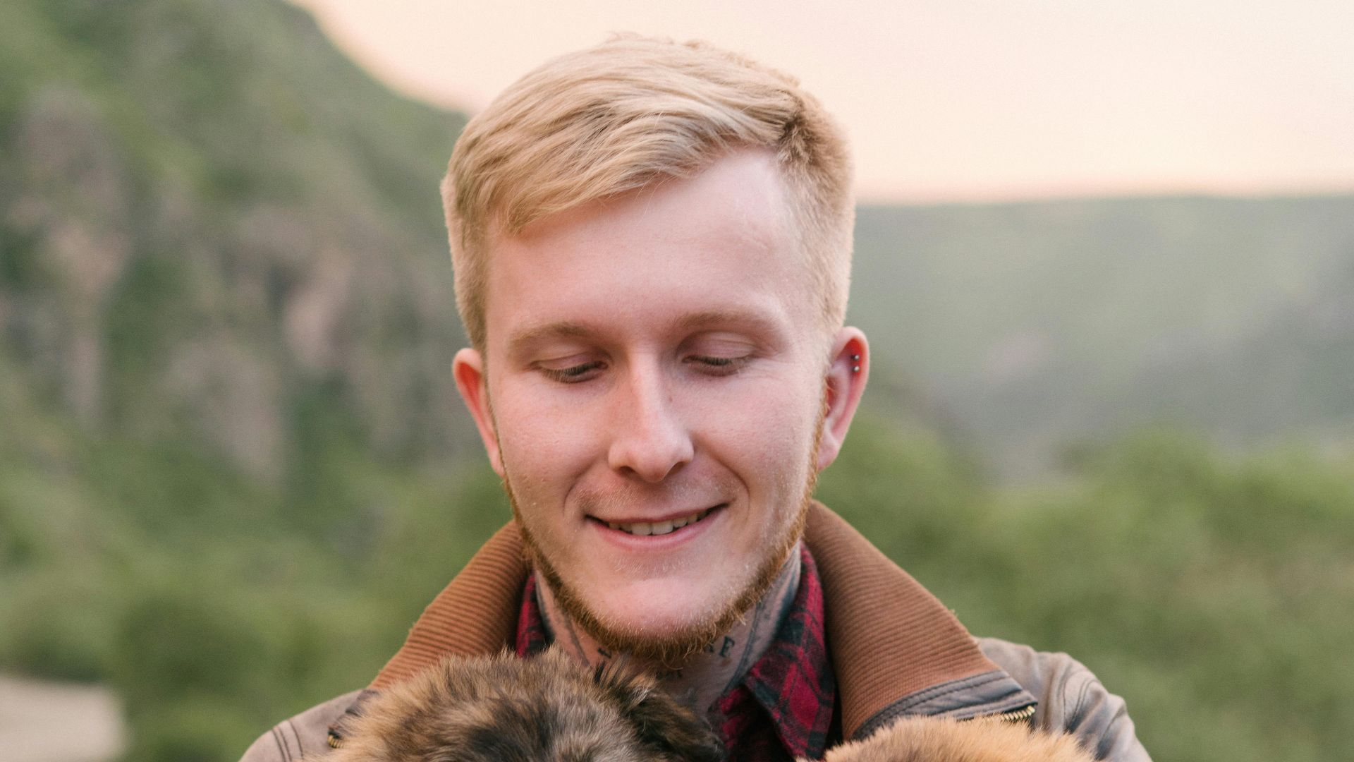 A happy man holding two adorable puppies in a scenic outdoor setting.