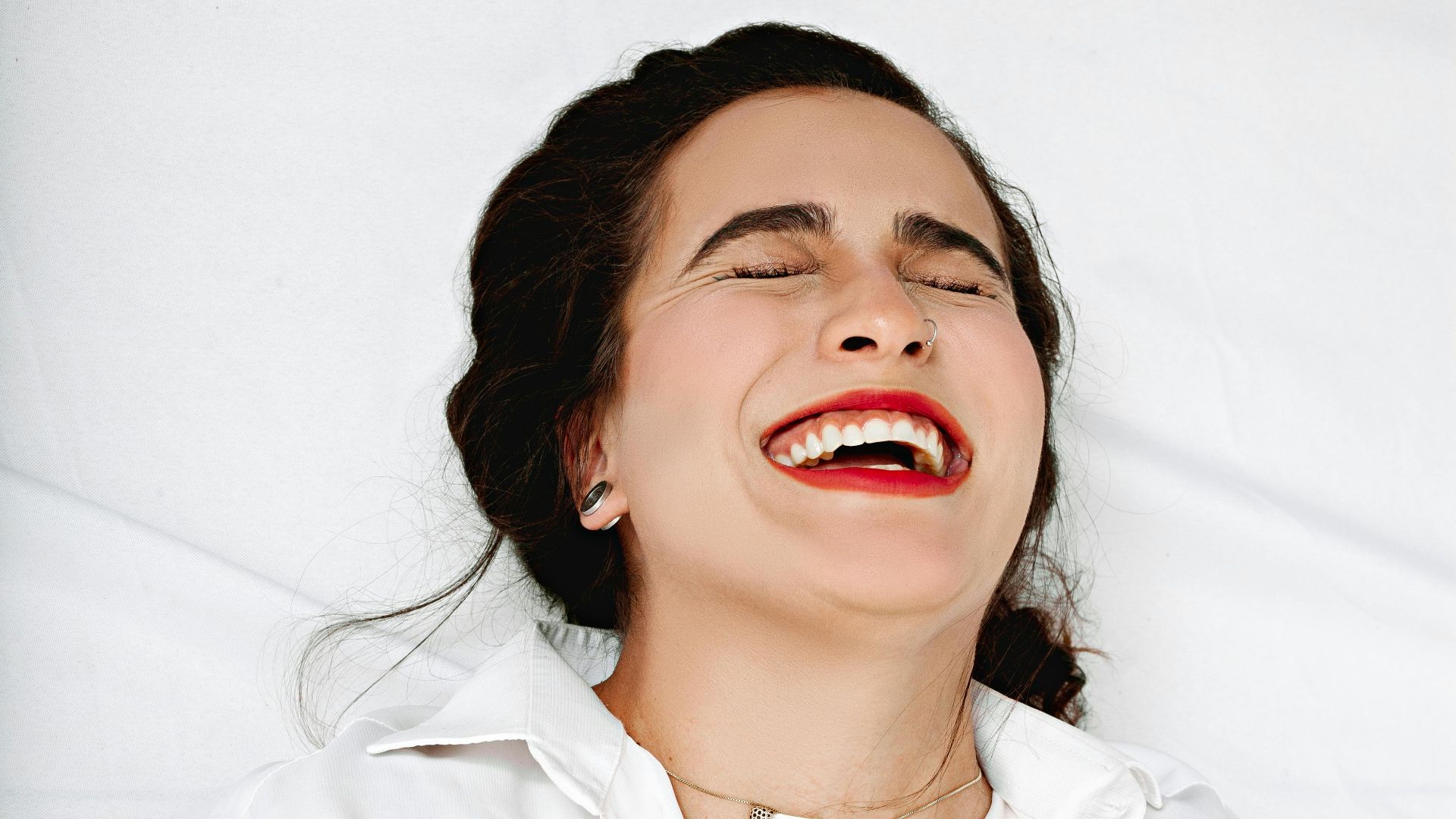 A woman in a white shirt joyfully laughs with her eyes closed, radiating happiness.