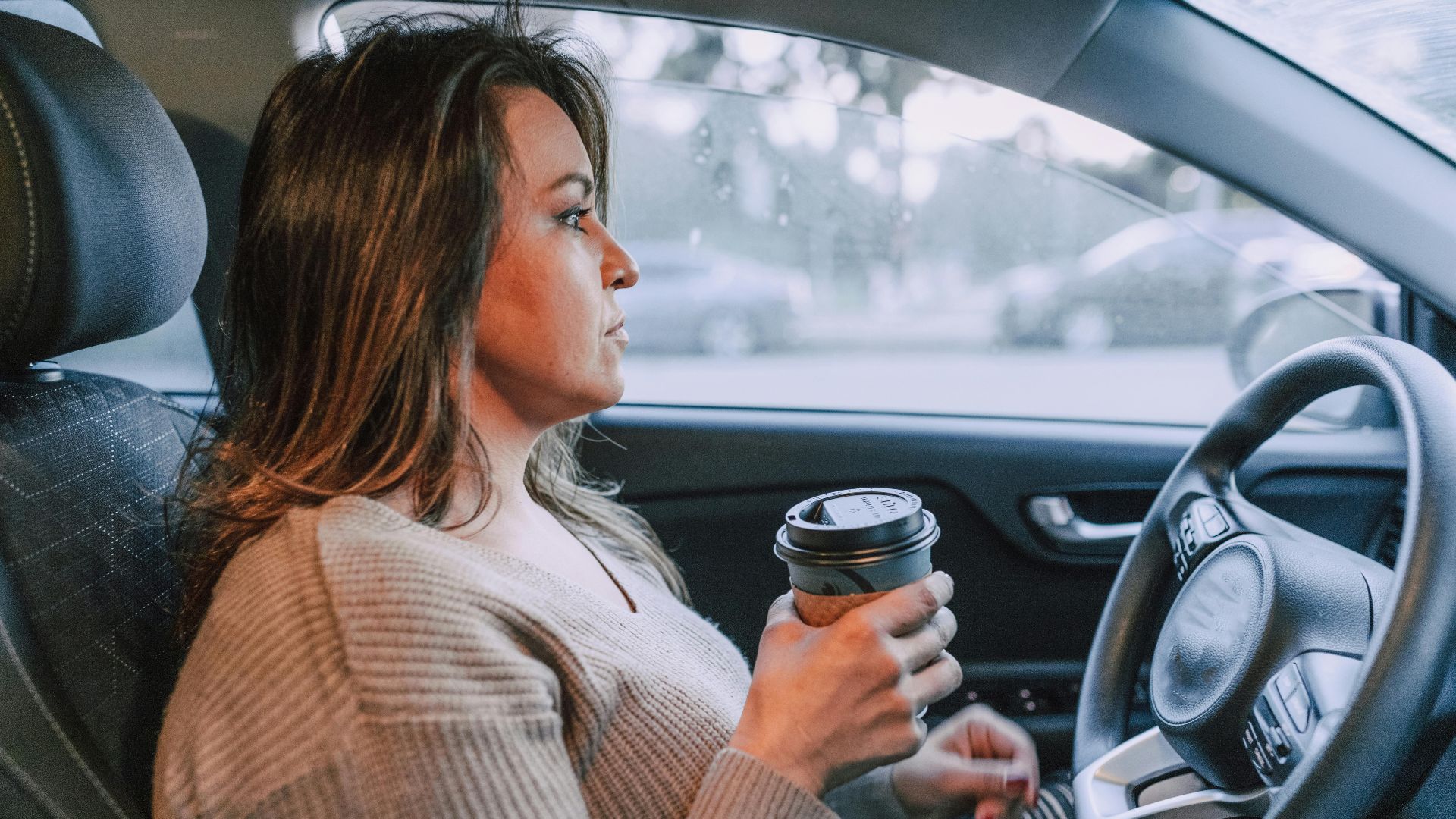 A woman in a car holding a disposable coffee cup, showing focus.