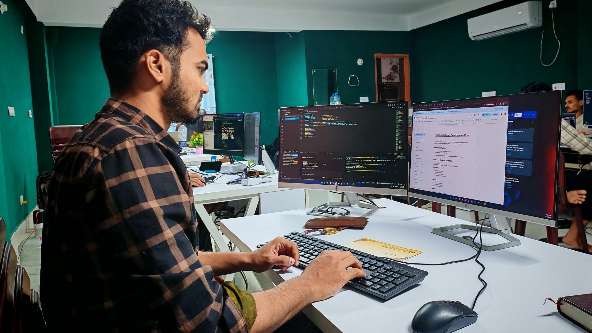 A software developer working on code at a dual monitor setup in a modern office.