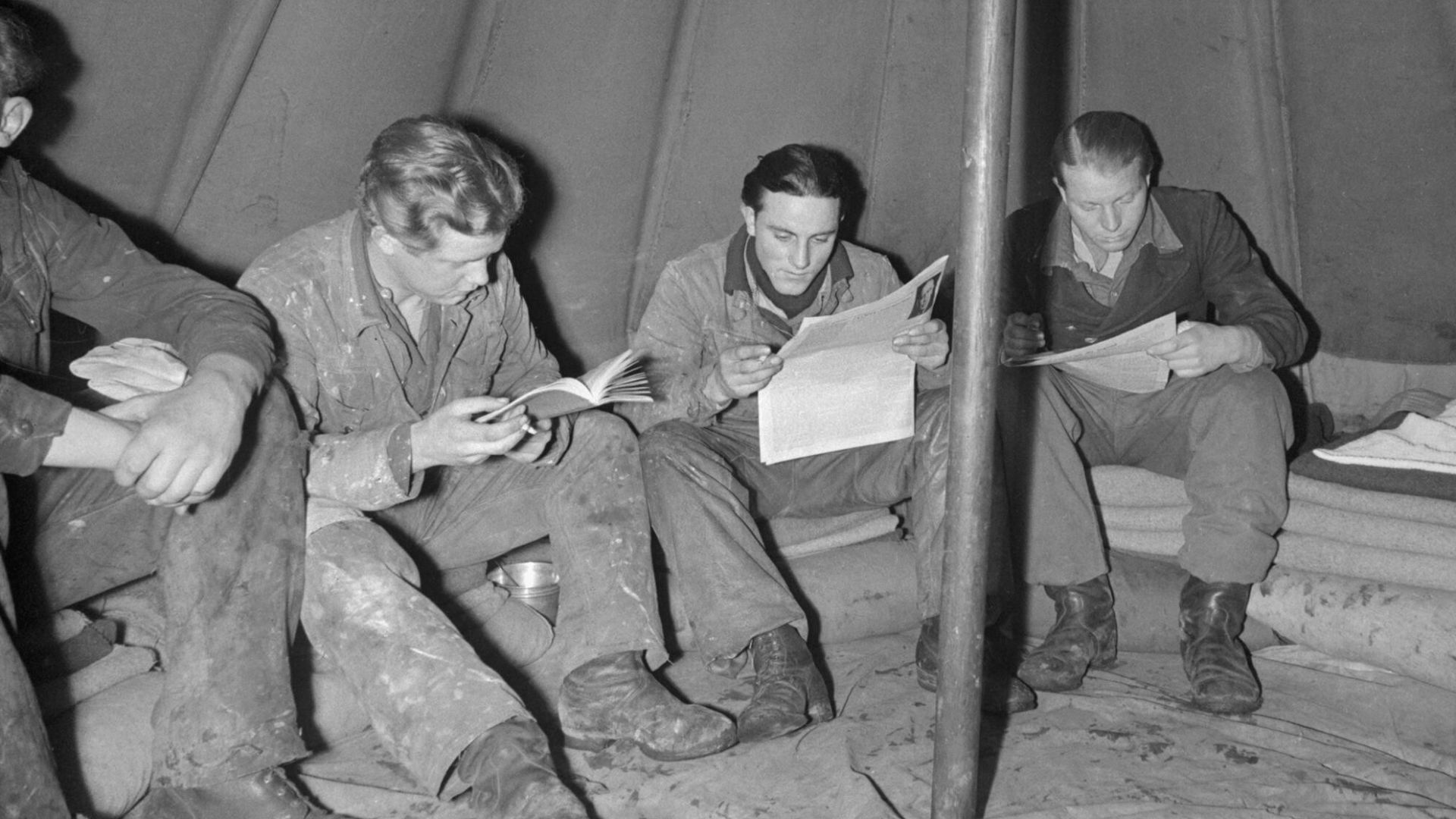 German Prisoners of War in Britain- Everyday Life at a German Pow Camp, UK, 1945
A group of German Prisoners of War read as they sit around the inside edge of a bell tent at a PoW camp, somewhere in Britain.  The large central pole which holds the tent up