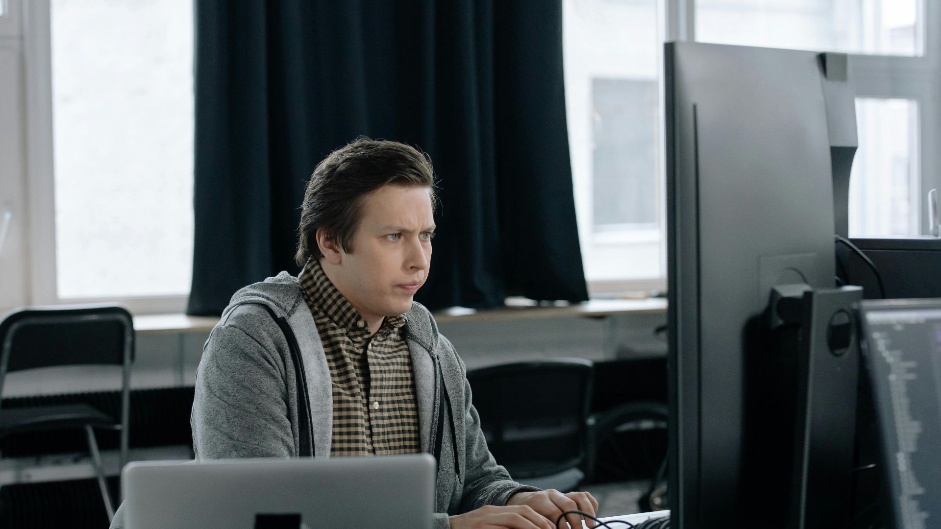 A dedicated programmer focused on coding at his workspace with dual monitors in a modern office setting.