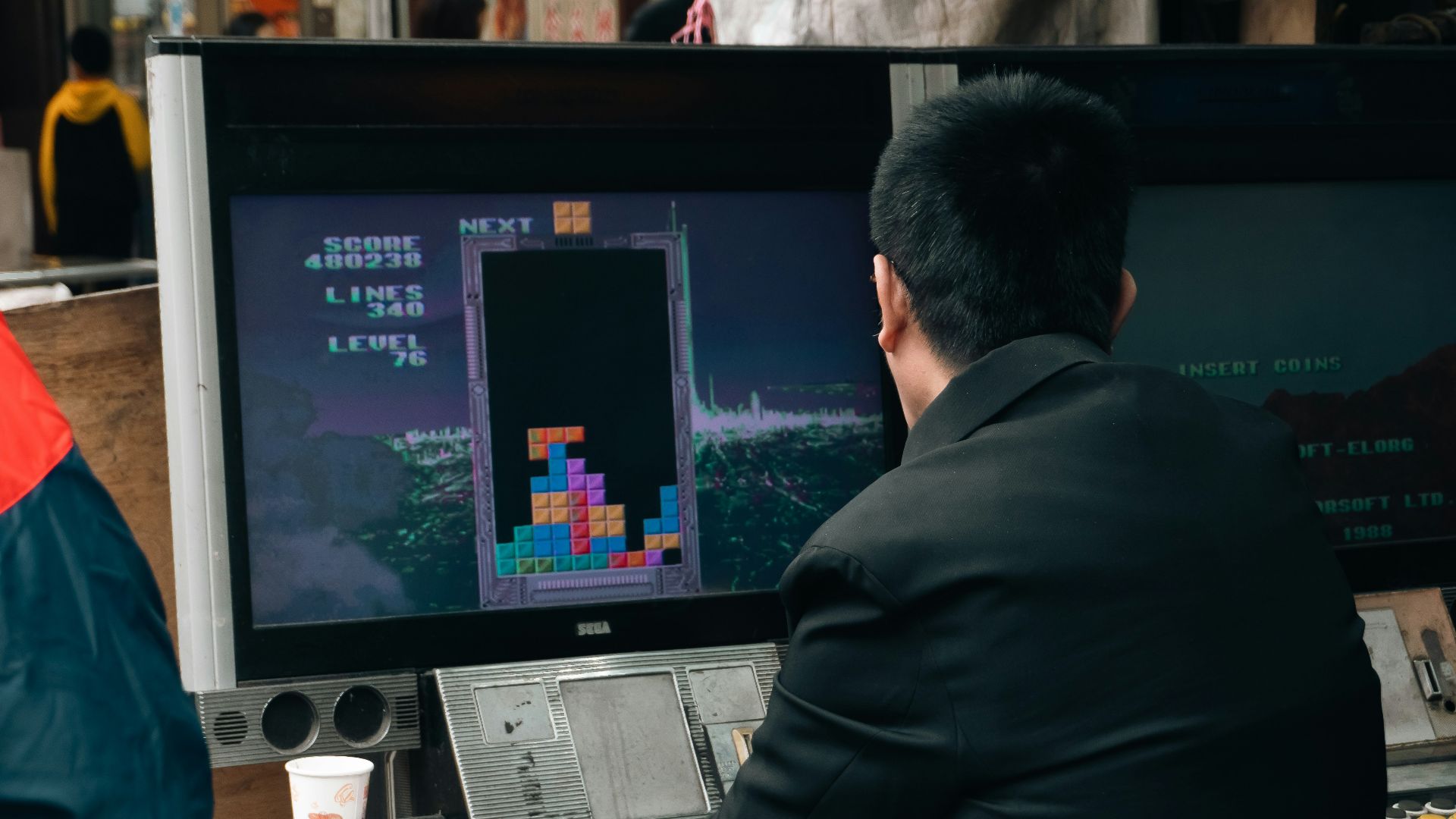 A man plays tetris on a vintage arcade game.
