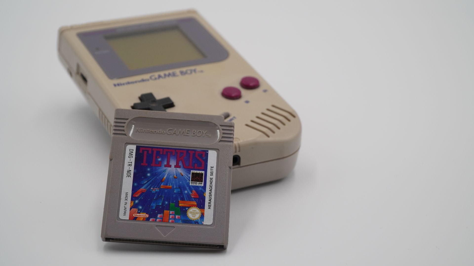 This picture shows a Nintendo Game Boy with a Tetris game cartridge leaned against it.