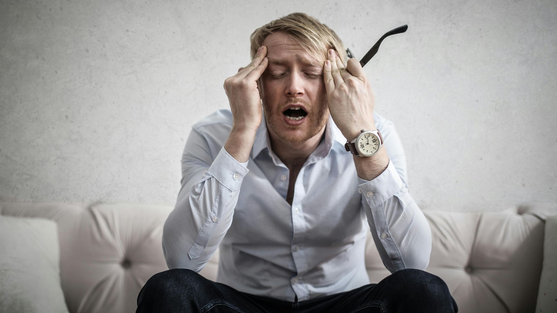 Stressed man sitting on couch, feeling overwhelmed and frustrated, expressing mental strain.