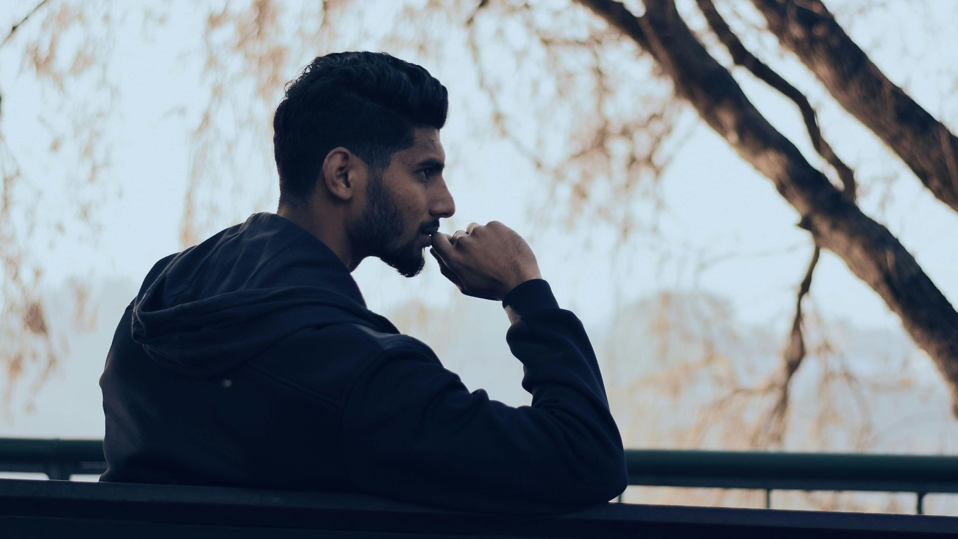 Man in deep thought sitting on a bench in a serene autumn park setting.