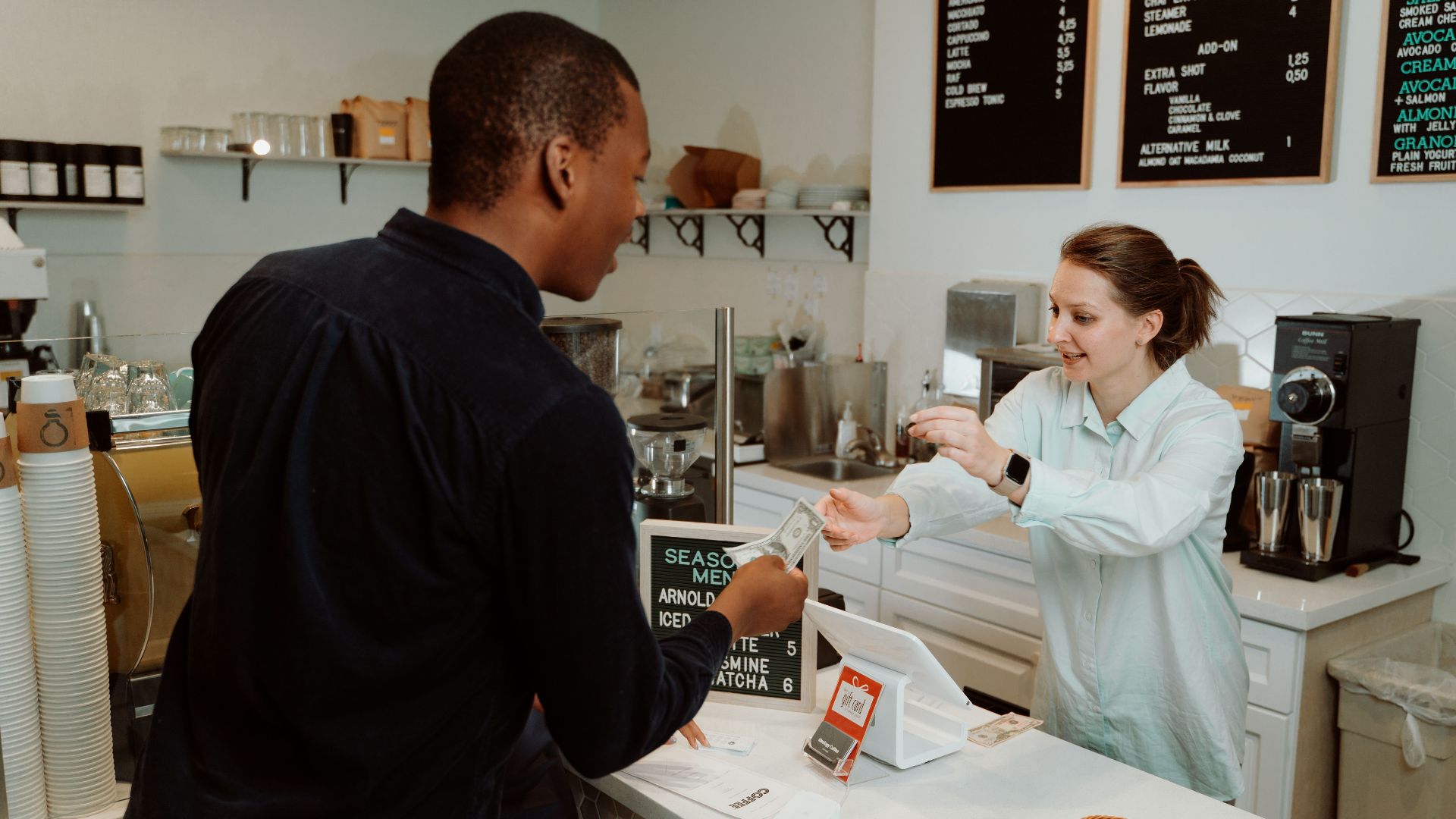 A customer pays for coffee at a café counter, transaction with barista.