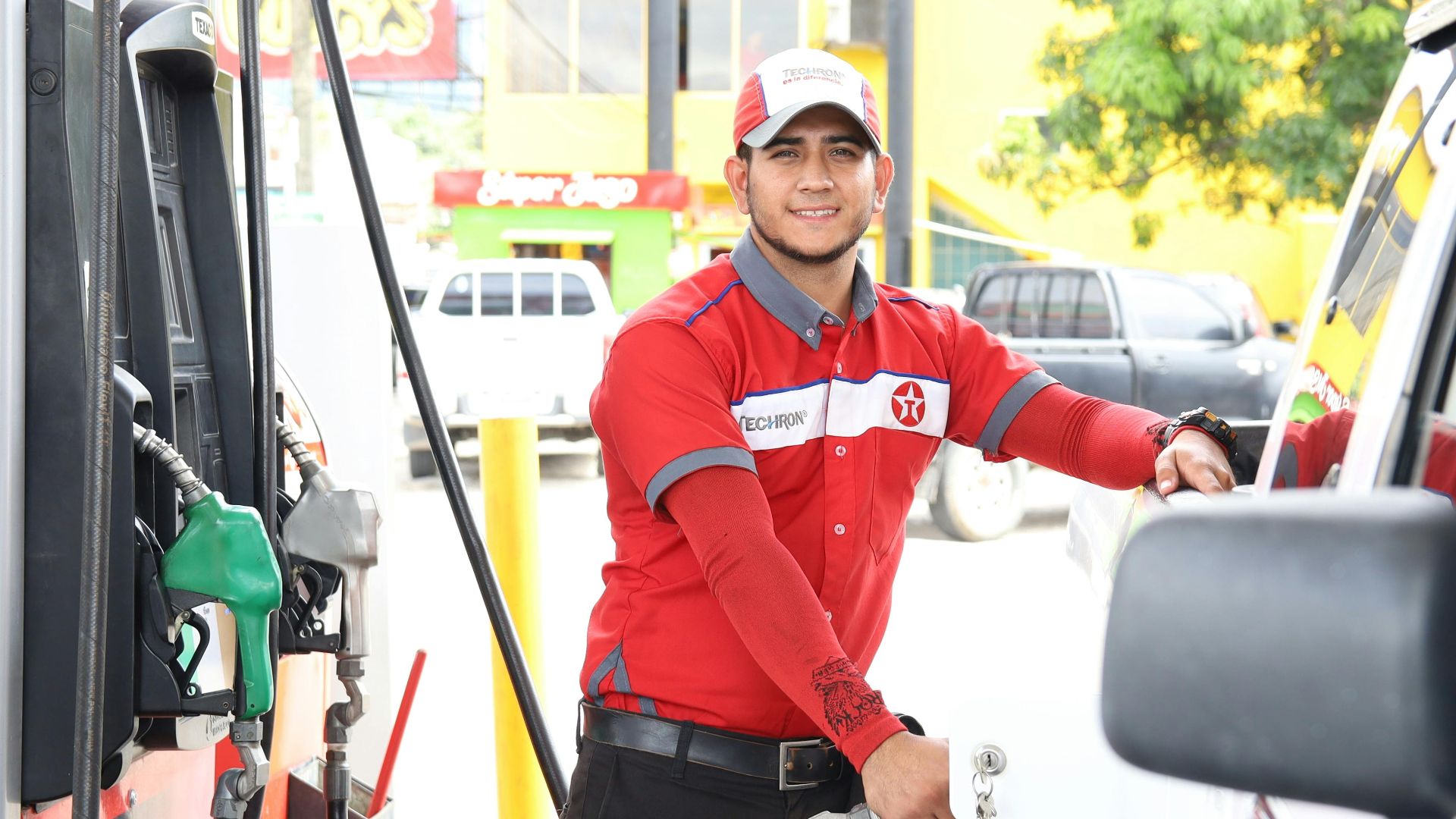 Cheerful gas station attendant refueling a car during the day.