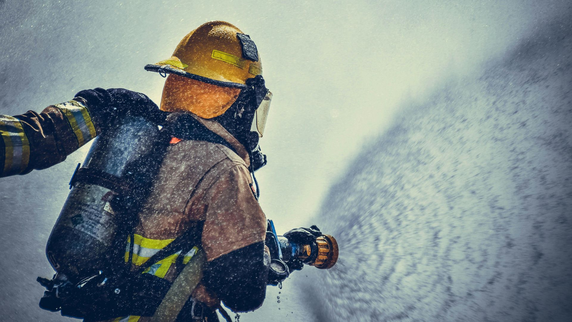 A brave firefighter in protective gear sprays water during training or emergency.