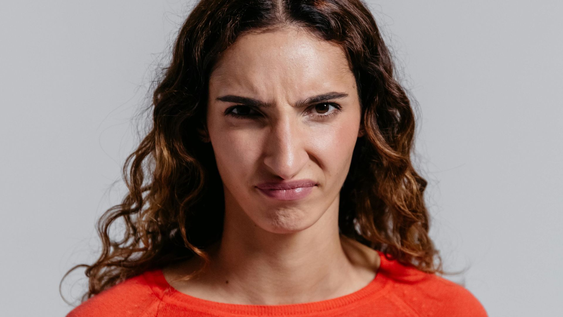 Portrait of a young woman in a red sweater showing an irritated facial expression in a studio setting.