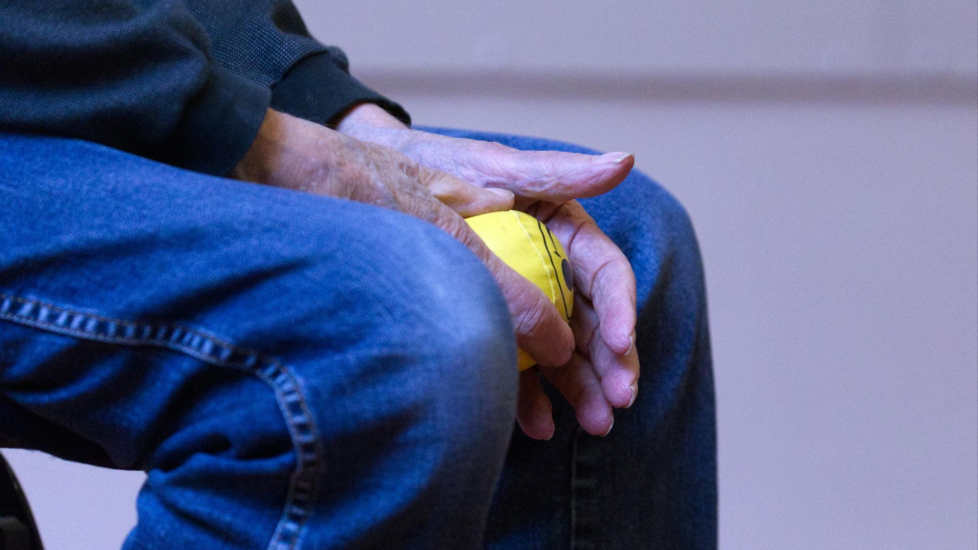 Elderly person holding a yellow stress ball in denim jeans, symbolizing relaxation and comfort.