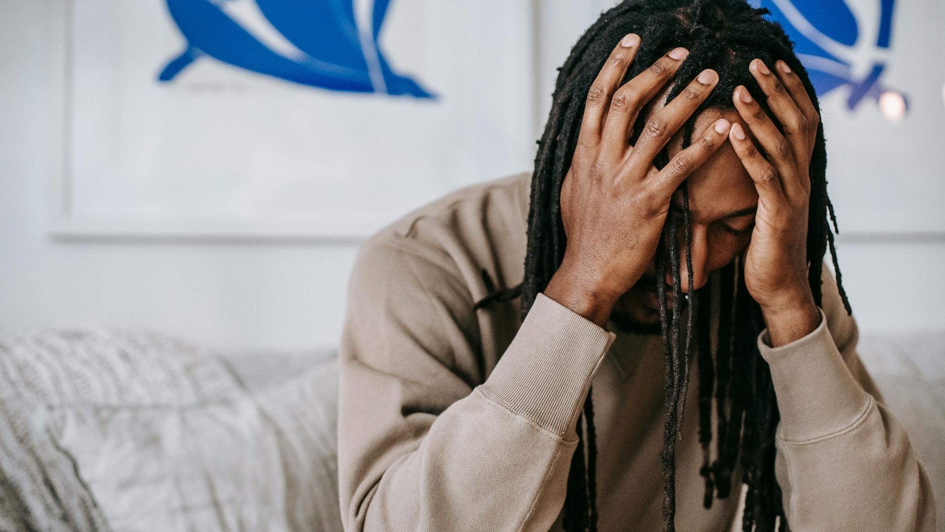 Crop anxious African American male with dreadlocks touching head with closed eyes on couch in house