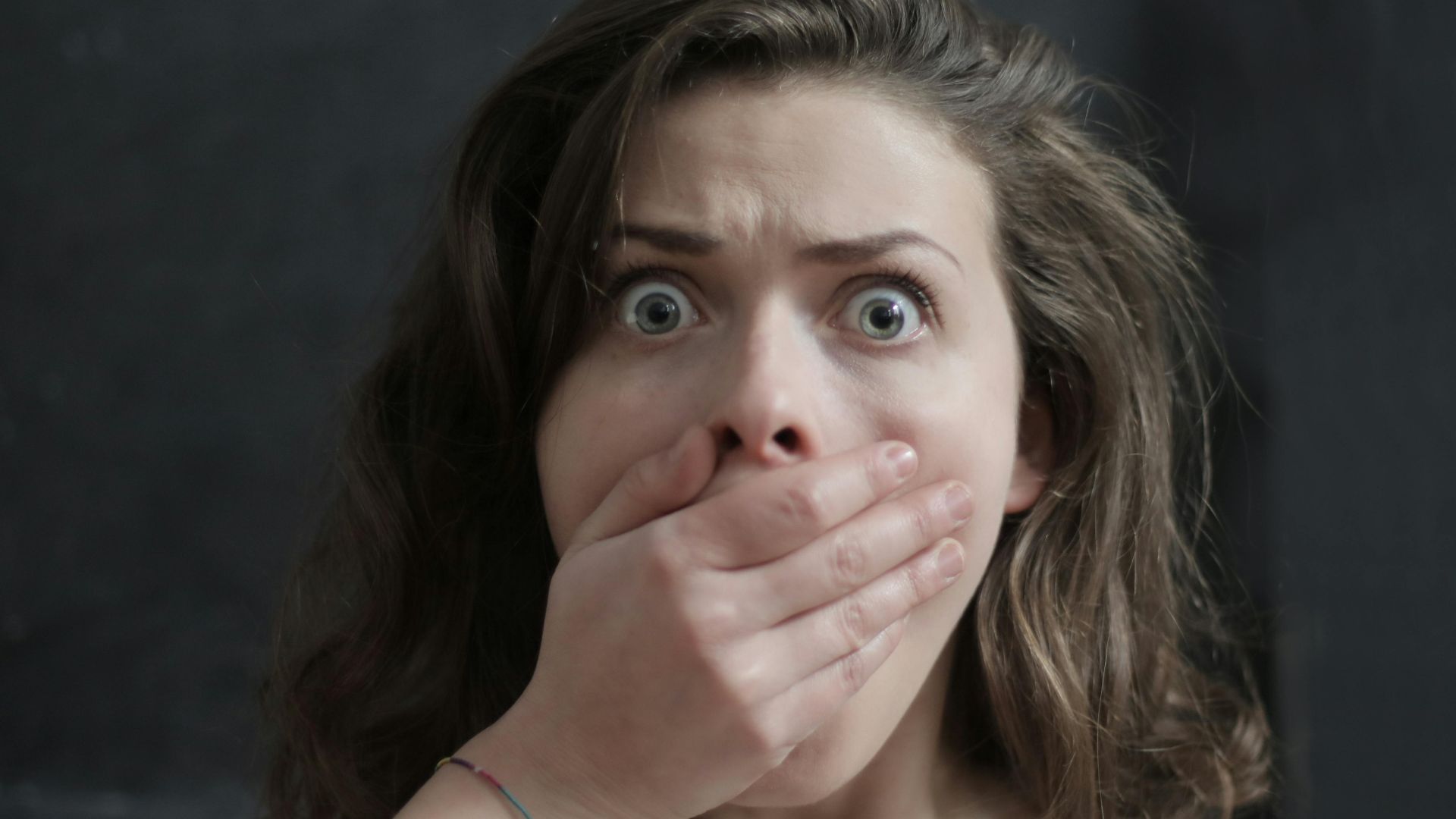 Close-up of a woman with a shocked expression, covering her mouth with her hand. Emotional and intense moment.