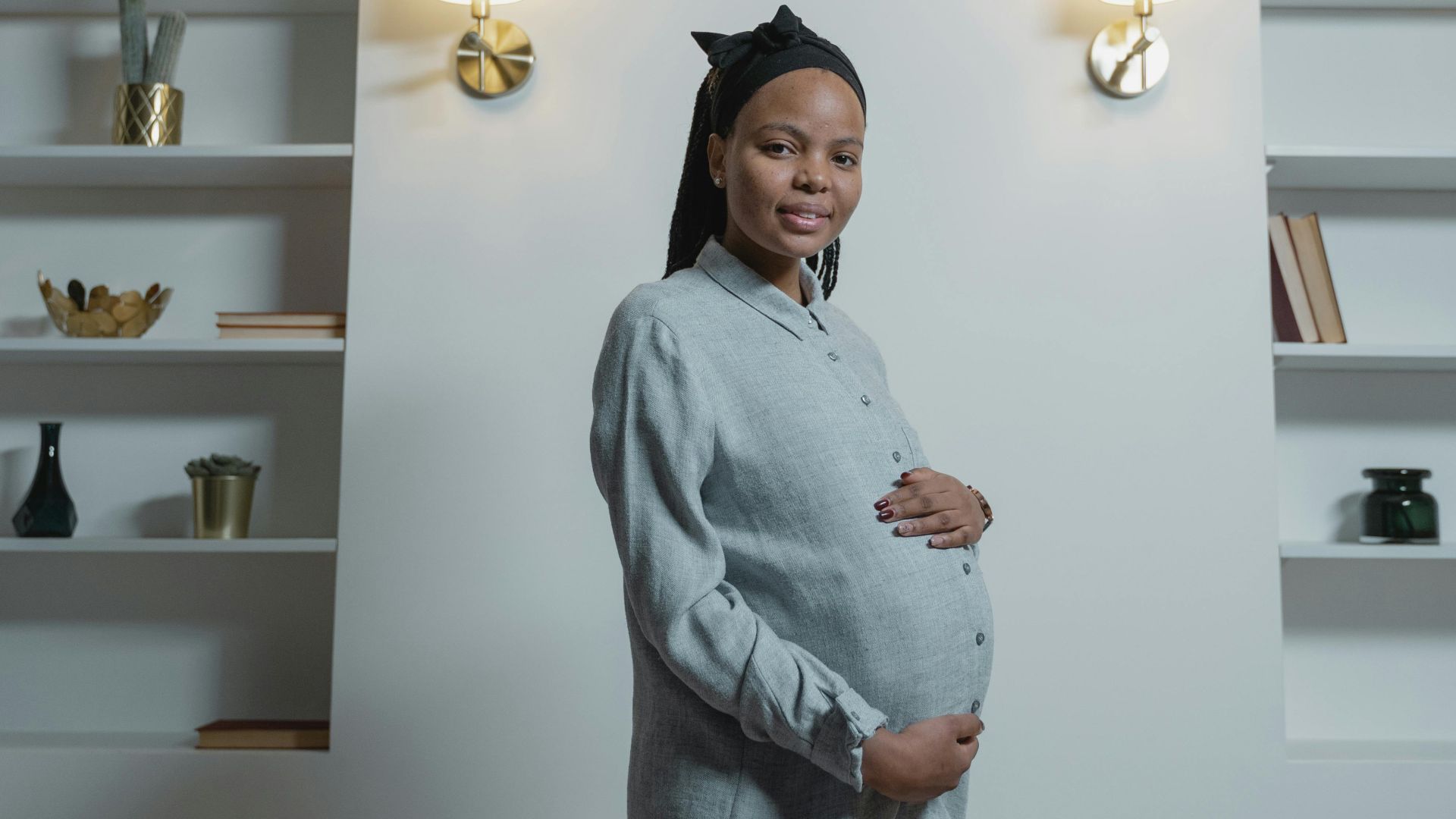 Pregnant woman smiling in a stylish room with bookshelves and wall lamps.