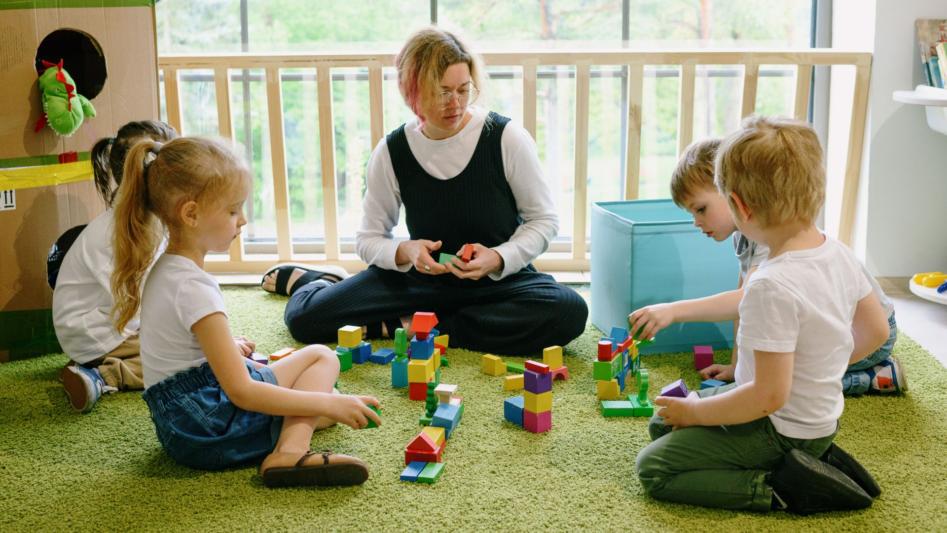 Children enjoying playtime with blocks and cardboard house in a cozy classroom.