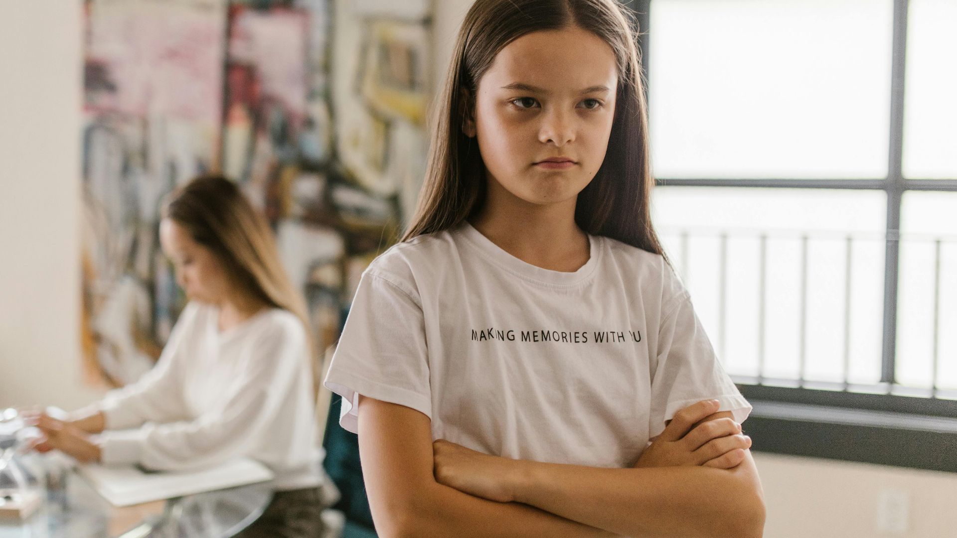 A young girl looks displeased with crossed arms in a modern indoor setting.