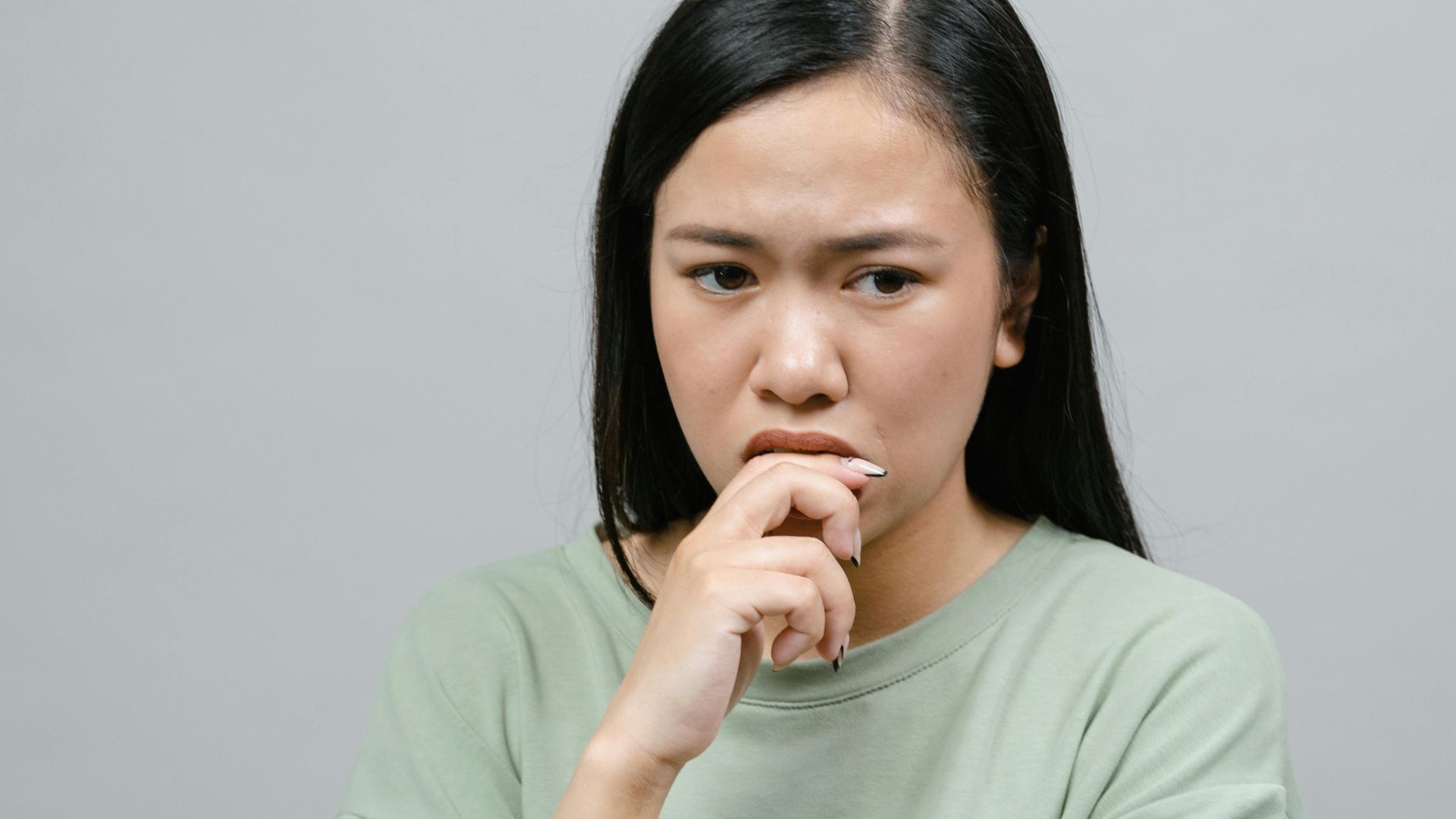Portrait of an Asian woman in a green shirt looking thoughtful against a gray backdrop.