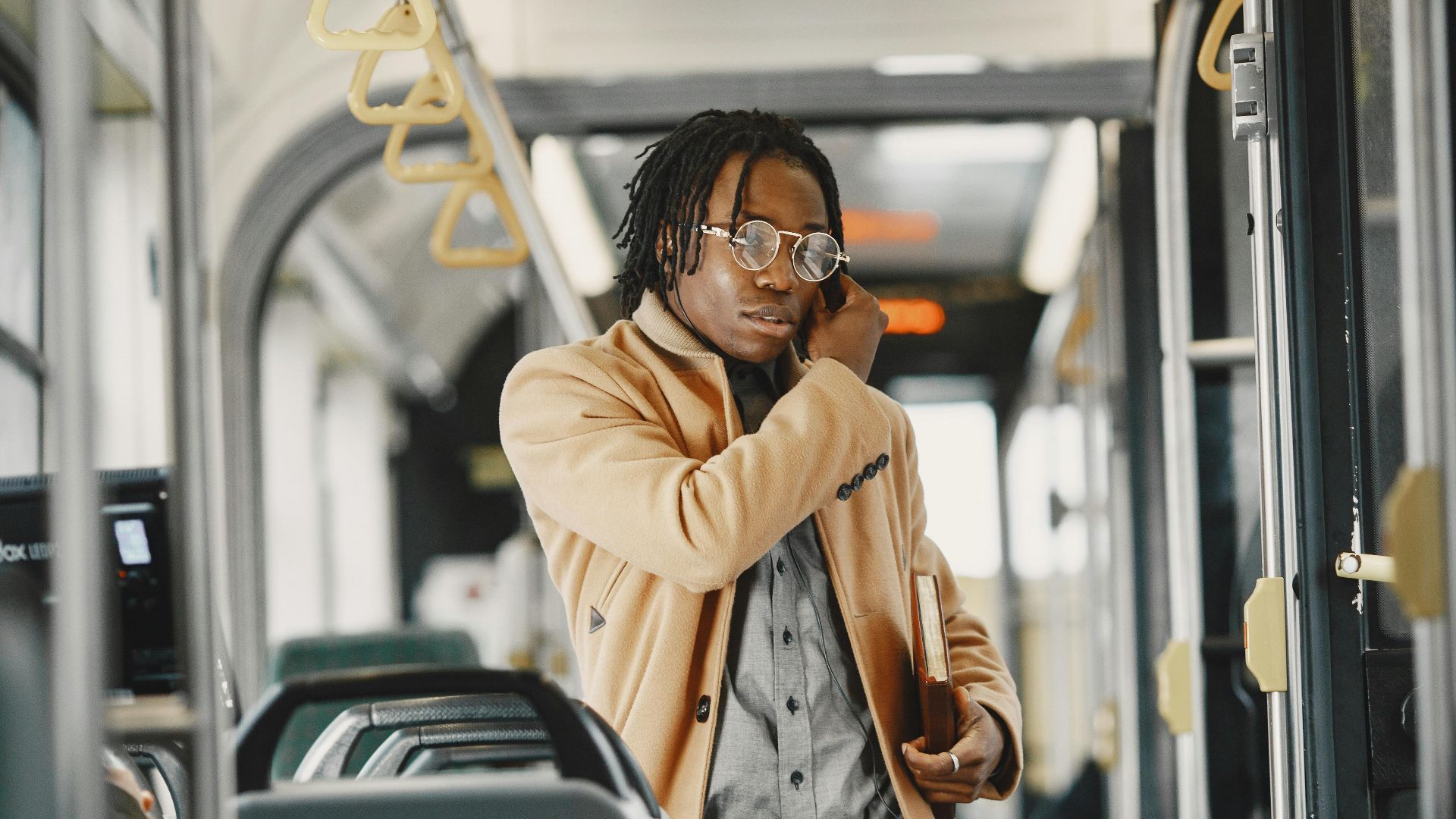 Stylish young man in a brown coat talking on his phone while commuting on a city bus.