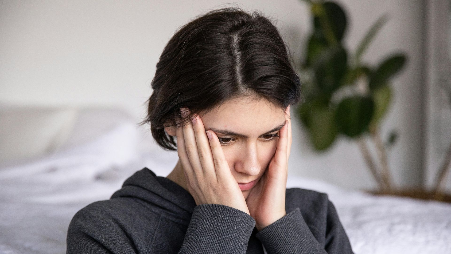Woman sitting indoors in thought, wearing a hoodie. Expressions of contemplation and introspection.