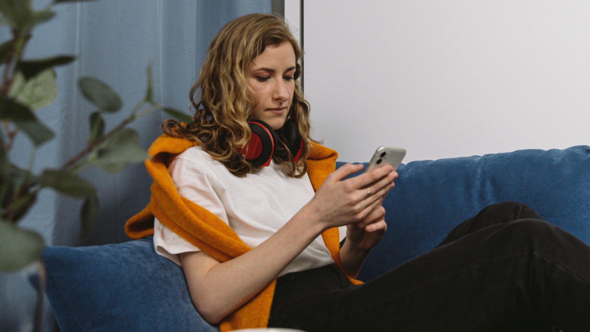 A woman sitting on a blue sofa using a smartphone, with a modern home setting.