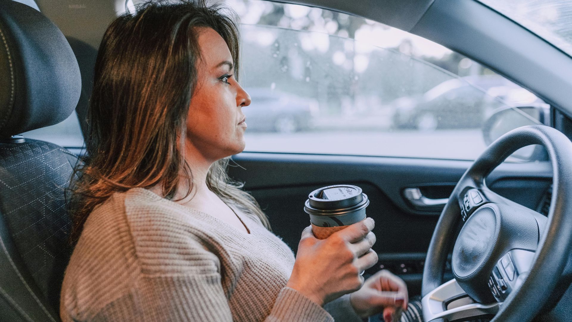 A woman in a car holding a disposable coffee cup, showing focus.