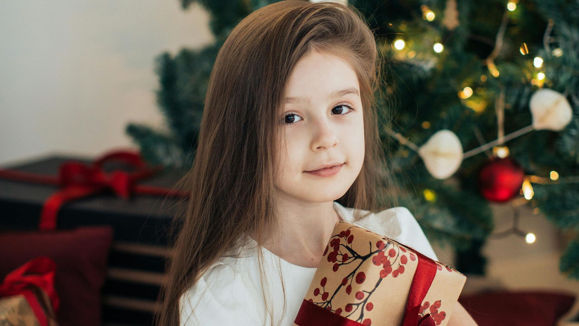 Smiling girl holding gift in front of a decorated Christmas tree