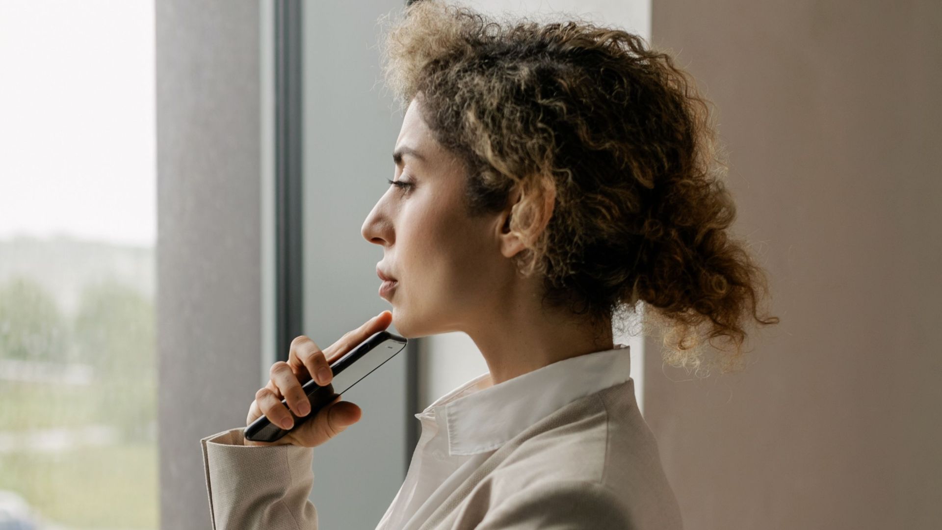 Professional woman in suit looking thoughtfully out a glass window, suggesting corporate environment.