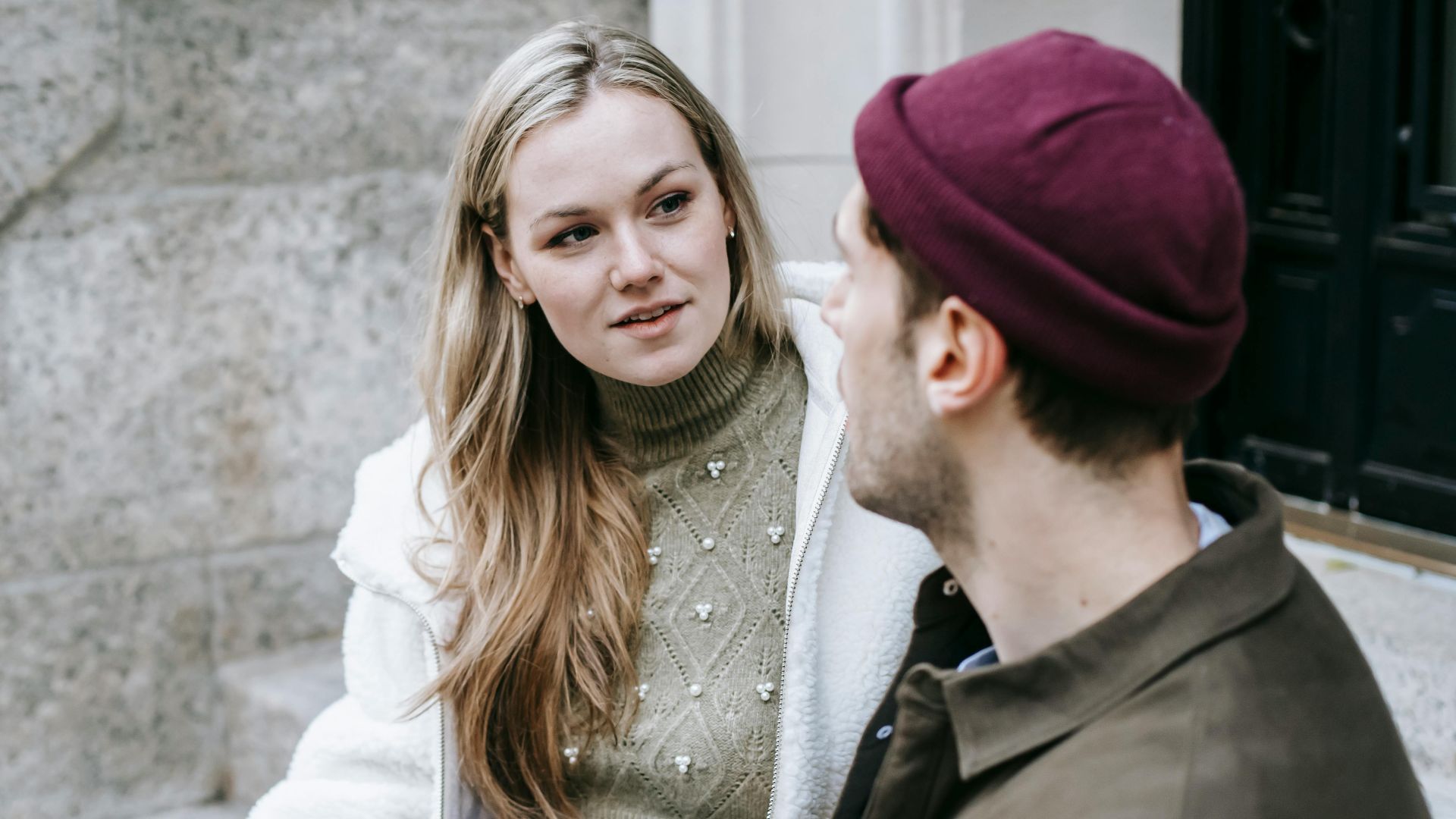 Man and woman talking sitting on steps outside house and having hot beverage in paper cups