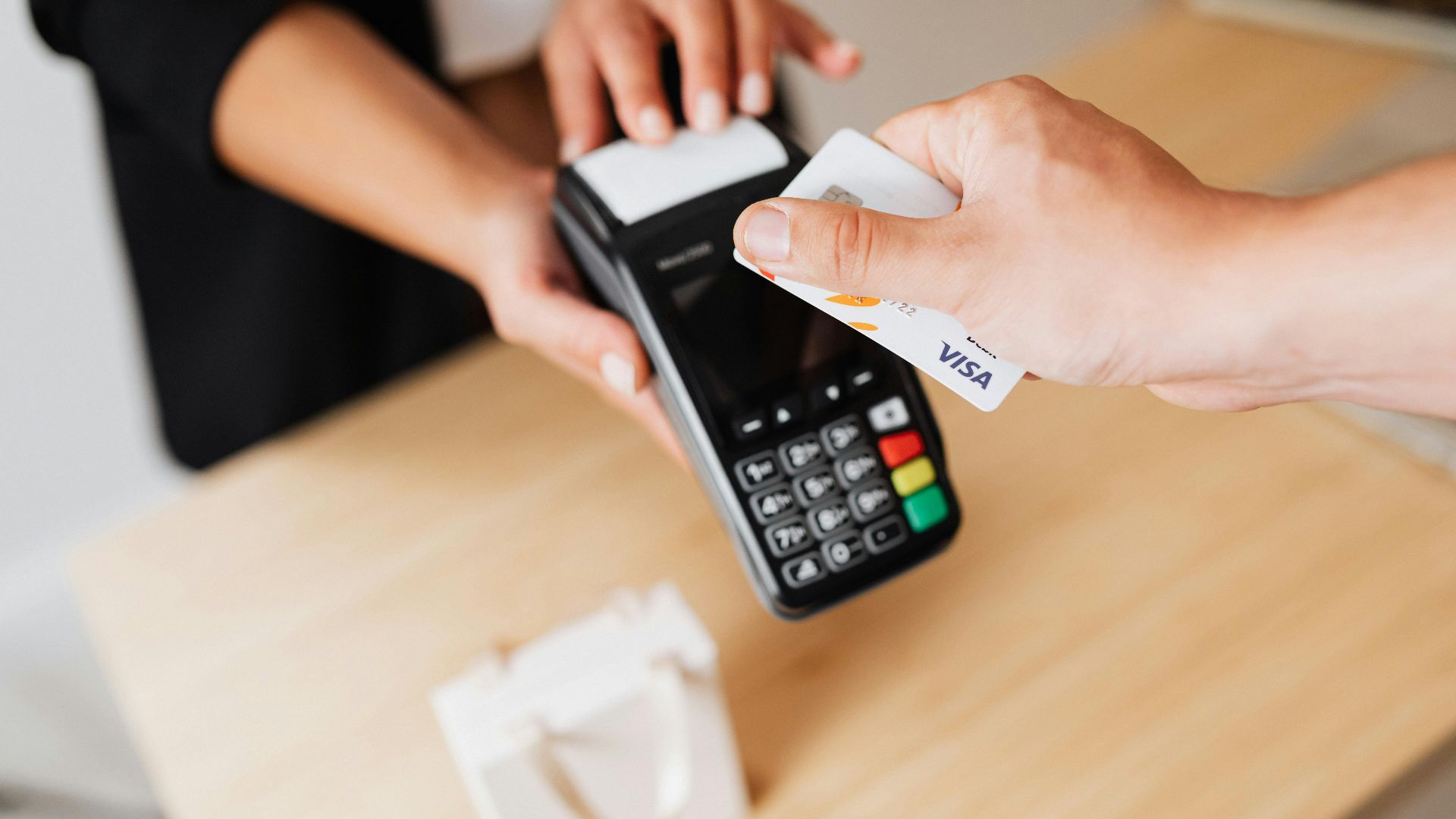 Close-up of hands using a contactless payment terminal with a credit card indoors.