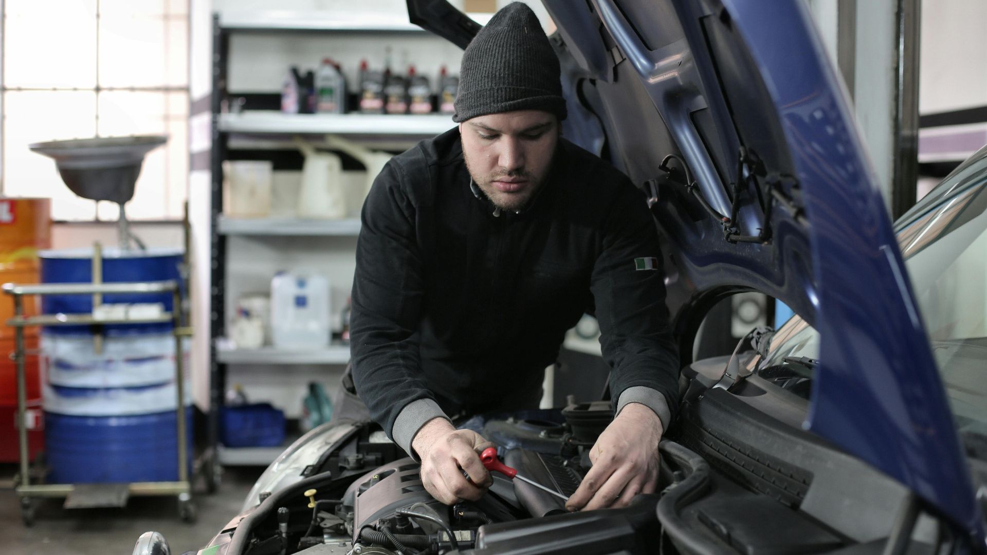 Man working under car hood in a garage, focused on engine repair