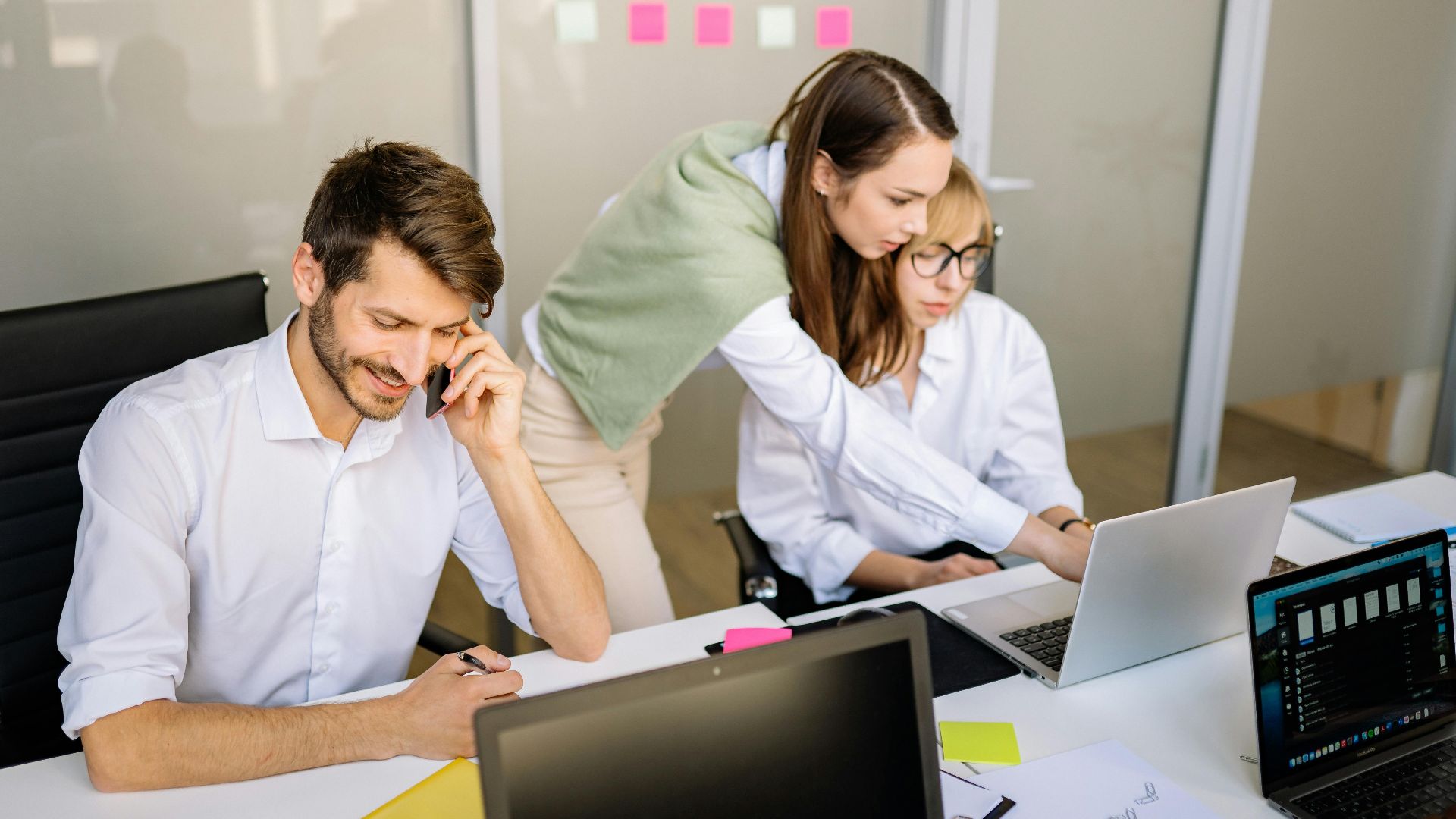 Three professionals engaged in teamwork at a conference table with laptops and notes.