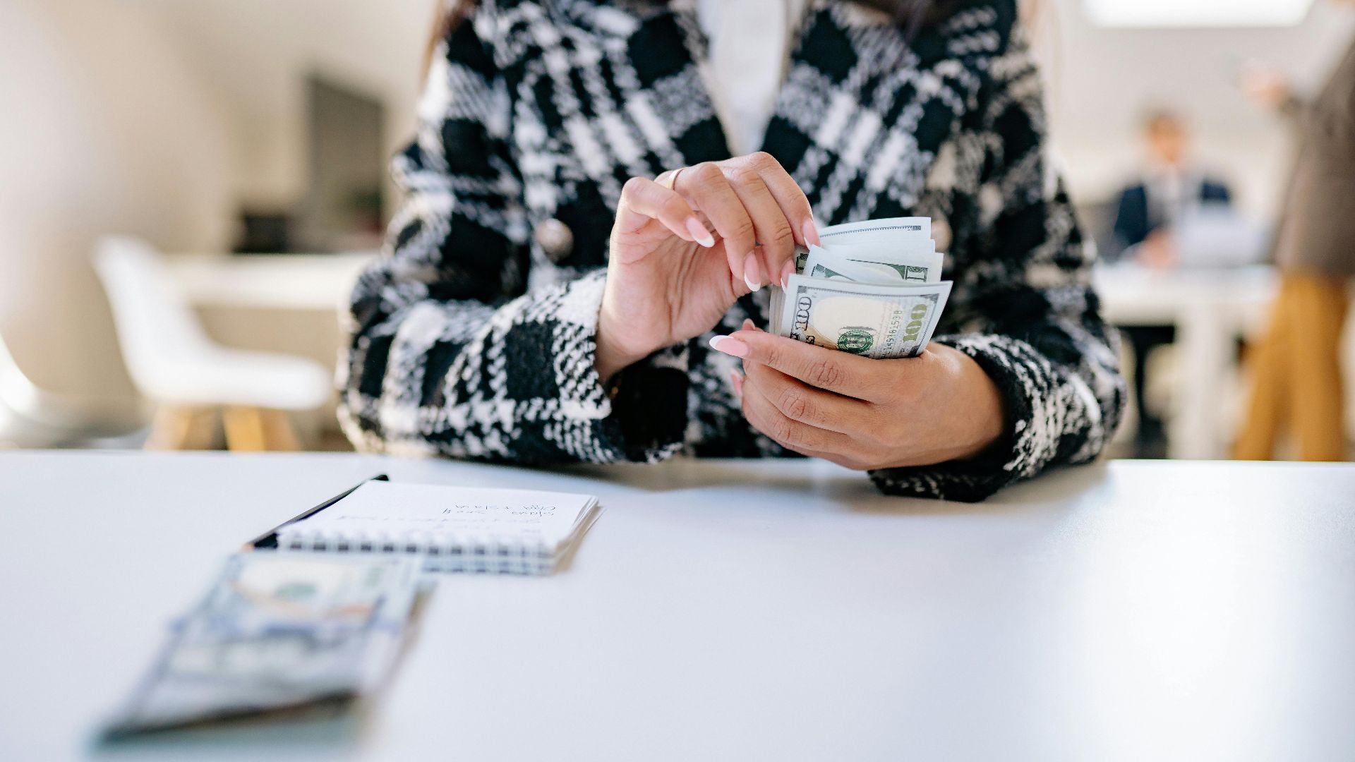 A close-up of a woman counting US dollars in an office environment, symbolizing financial management.