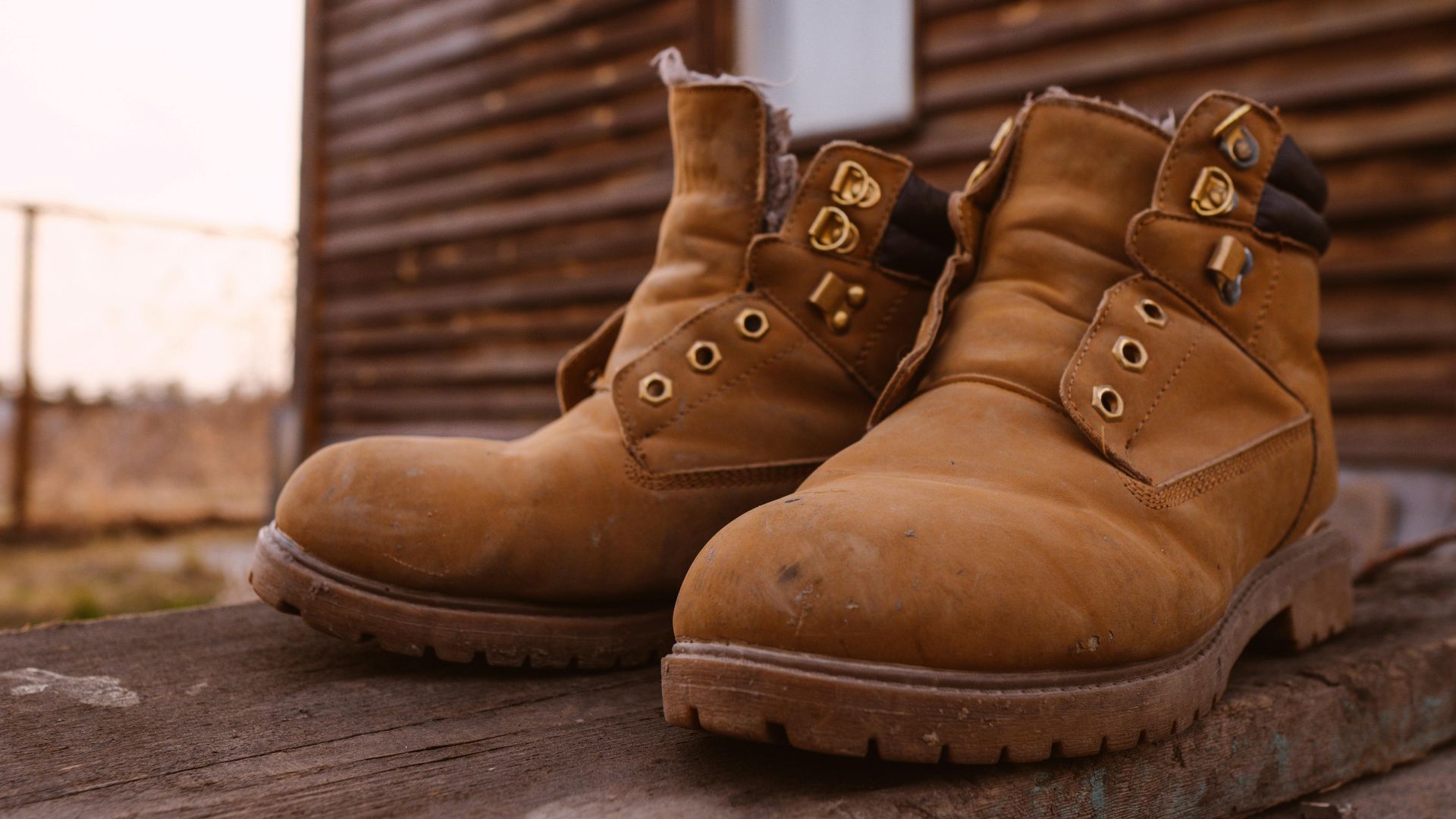 Close-up of rugged suede boots resting outside a rustic wooden cabin on a wooden platform.