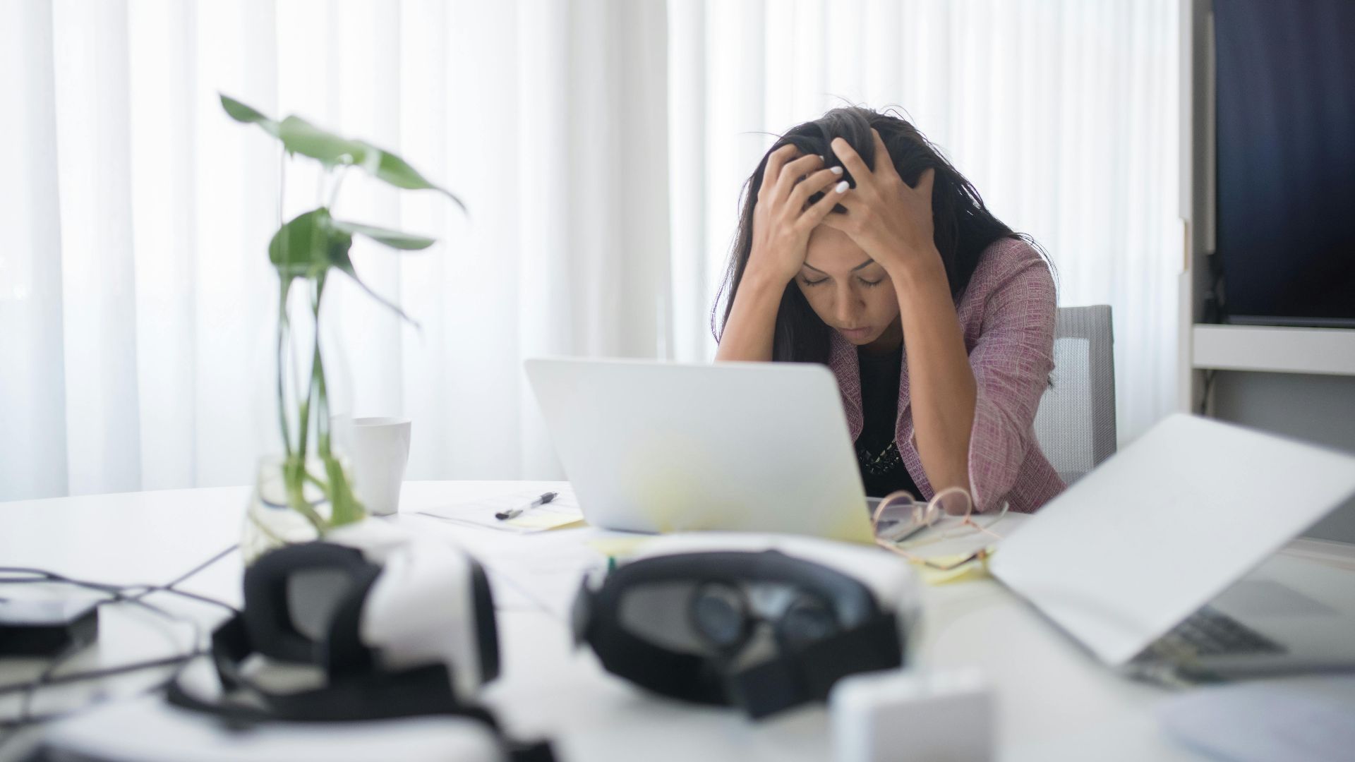Frustrated woman sitting at desk with laptop, showing stress in a modern office environment.