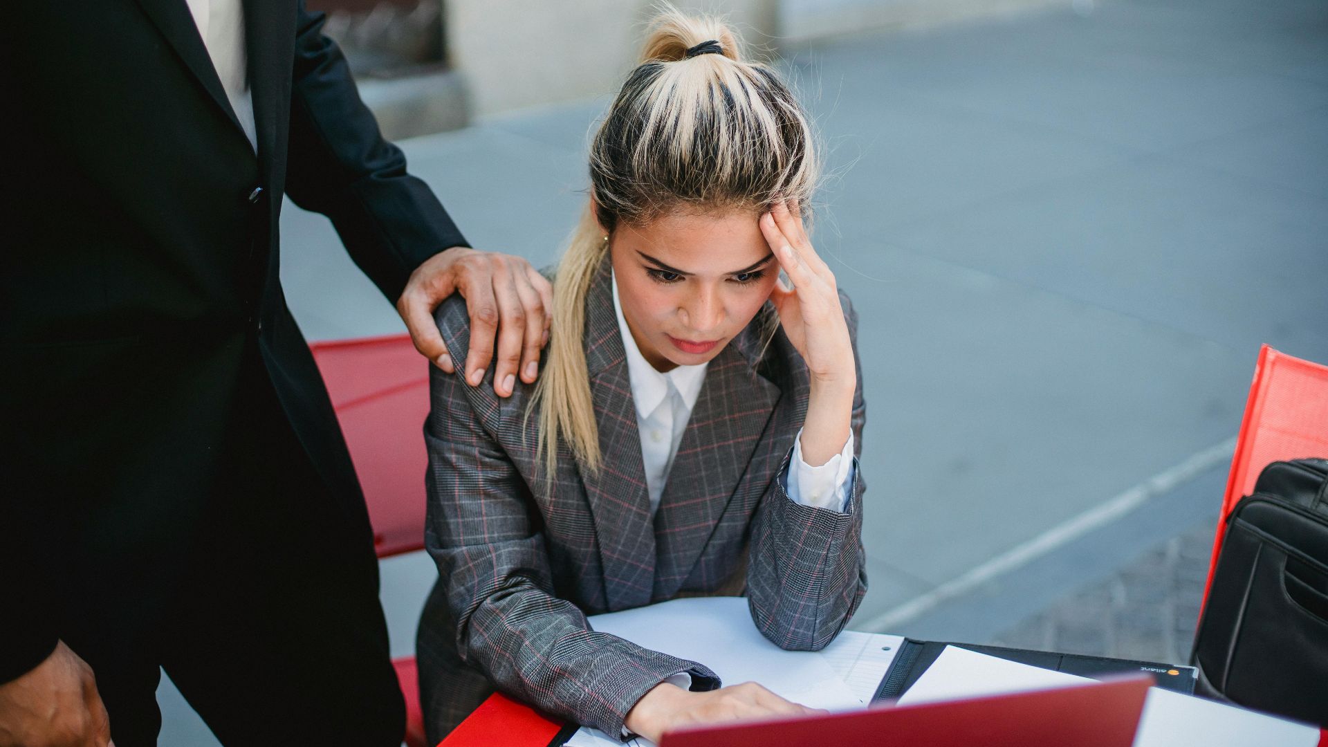 Businesswoman in stress at outdoor table, seeking support from colleague.