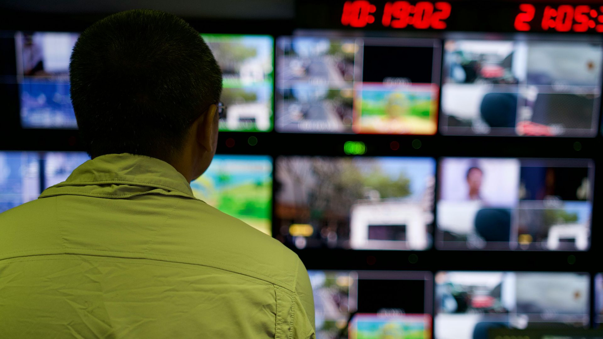 Man in a control room overseeing multiple monitors displaying various scenes.