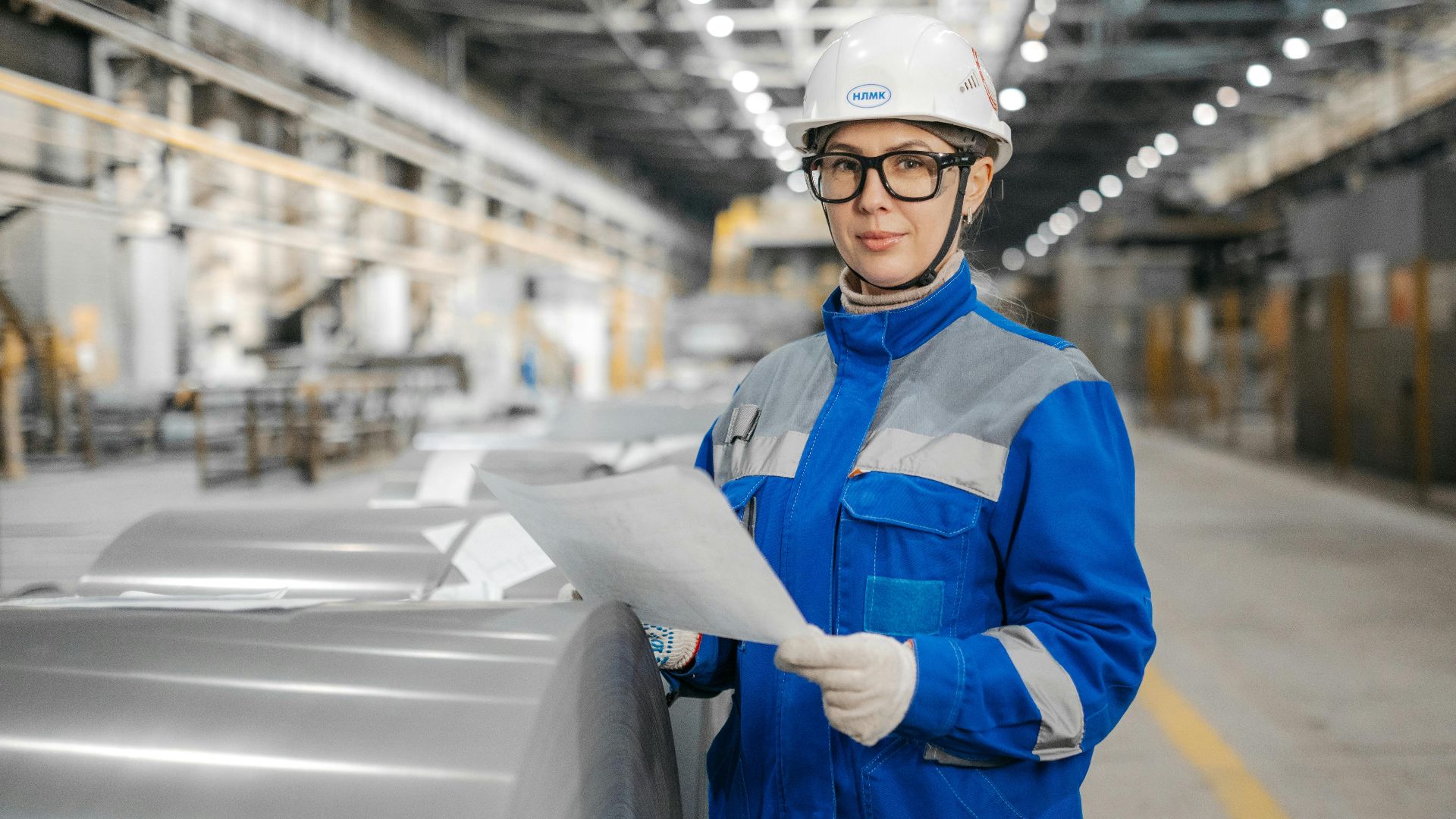 A female engineer wearing safety gear inspects machinery in an industrial factory setting.
