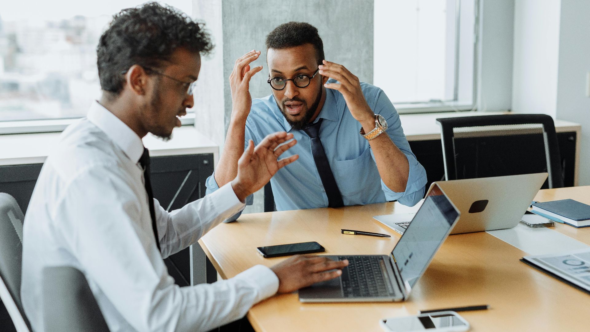 Two colleagues discussing a project with laptops during a brainstorming session in an office setting.