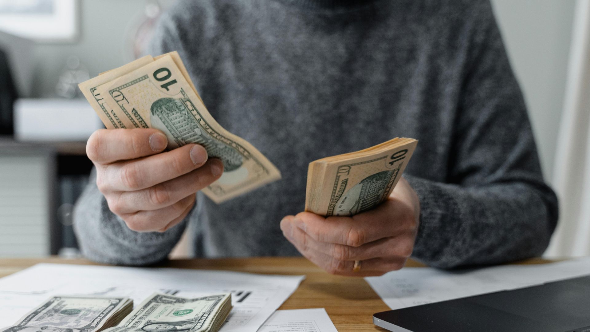 Close-up of person counting cash with a calculator and paperwork on a desk.