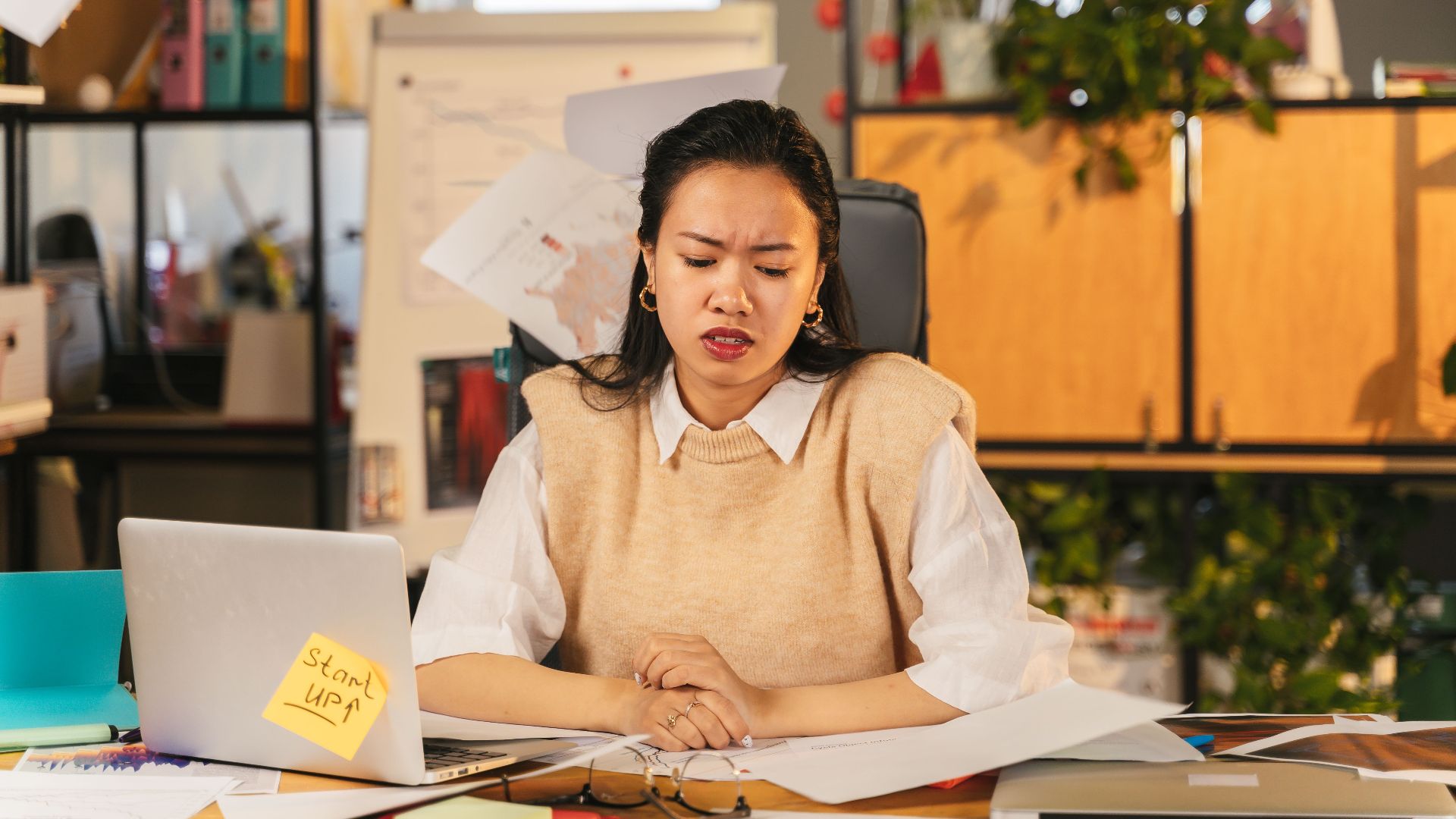 An office worker showing frustration while sitting at a cluttered desk with a laptop.