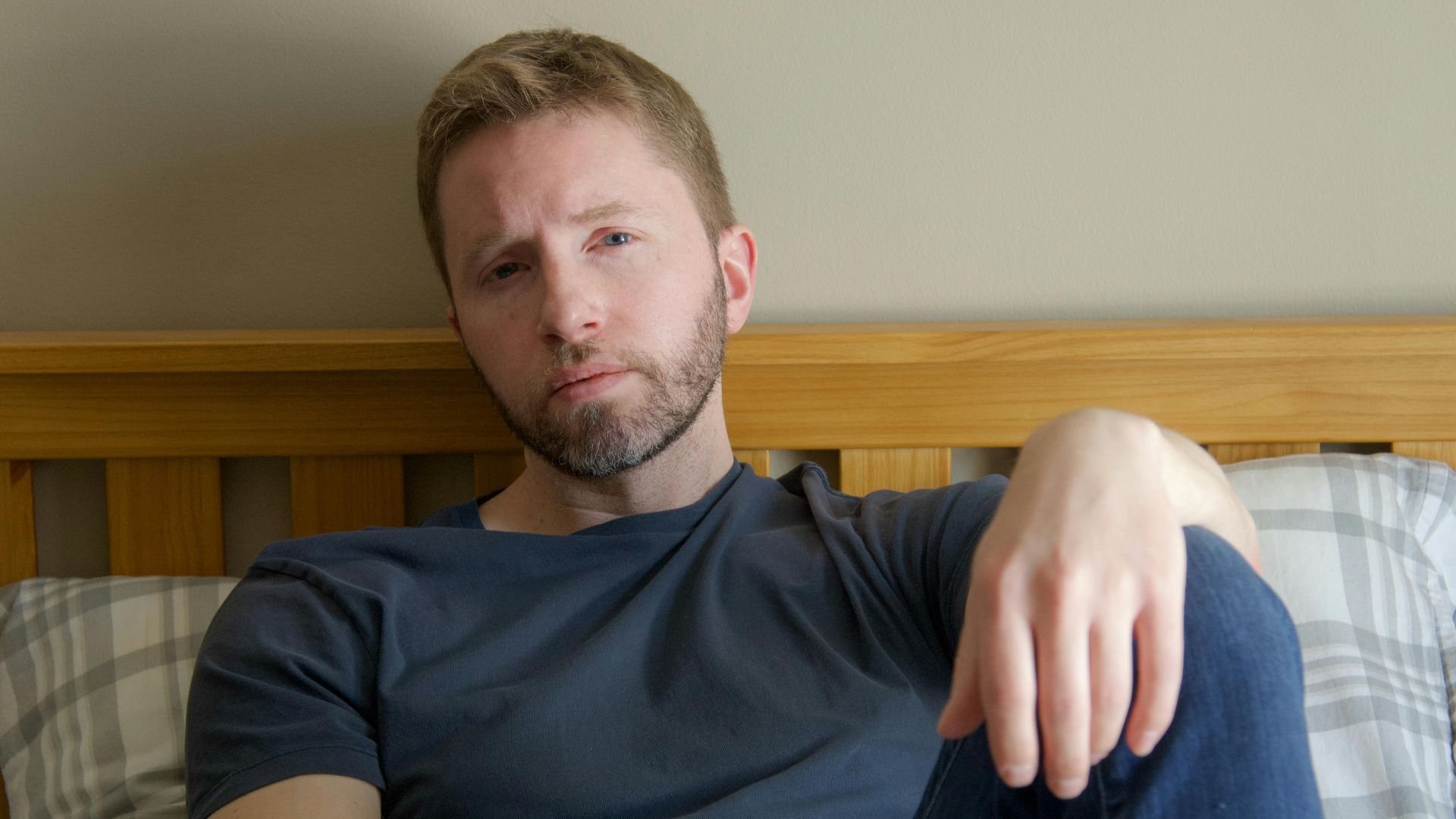 Man with contemplative look relaxing on bed at home, daytime lighting.